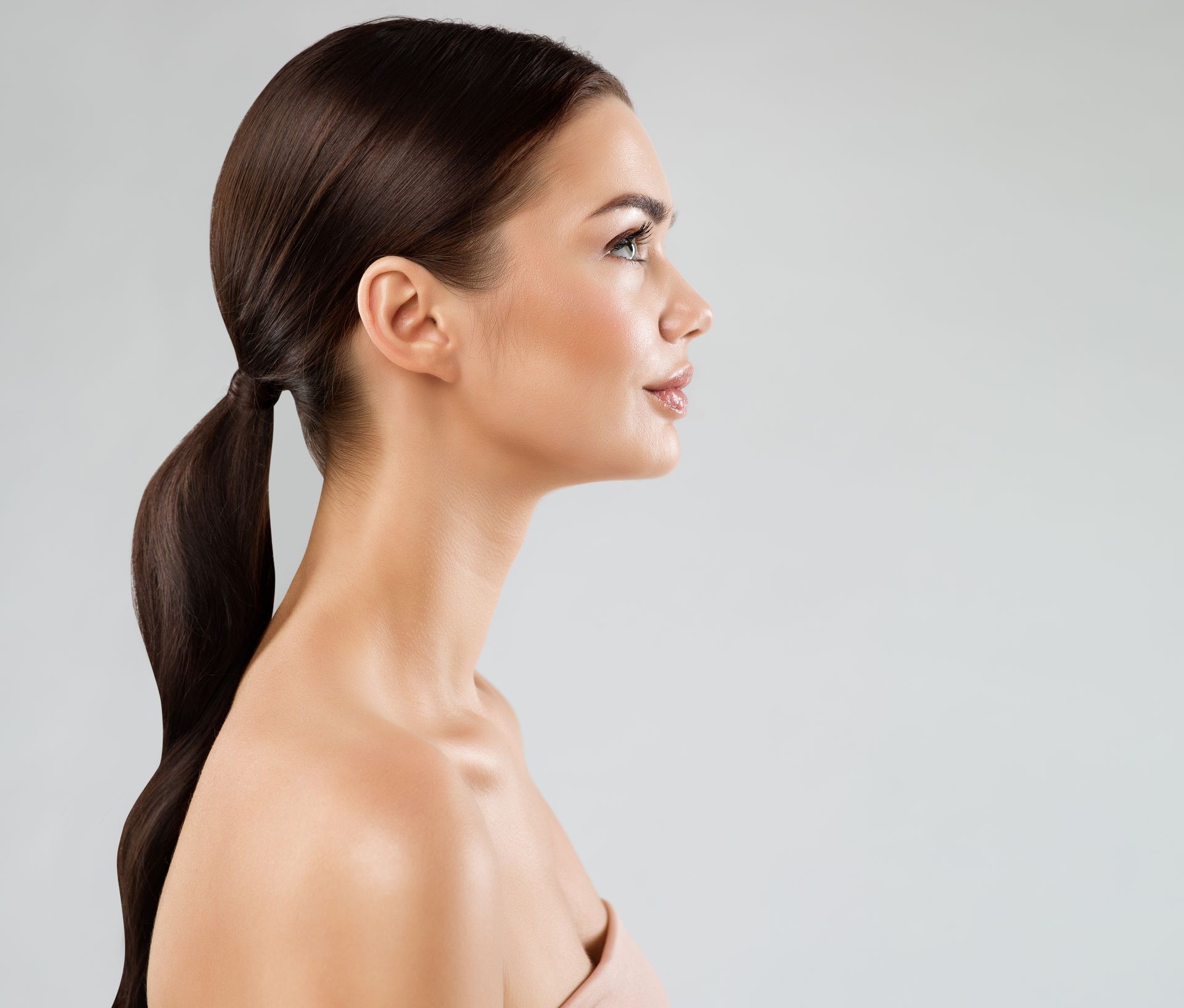 Profile portrait of a woman with dark hair in a low ponytail against a light gray background