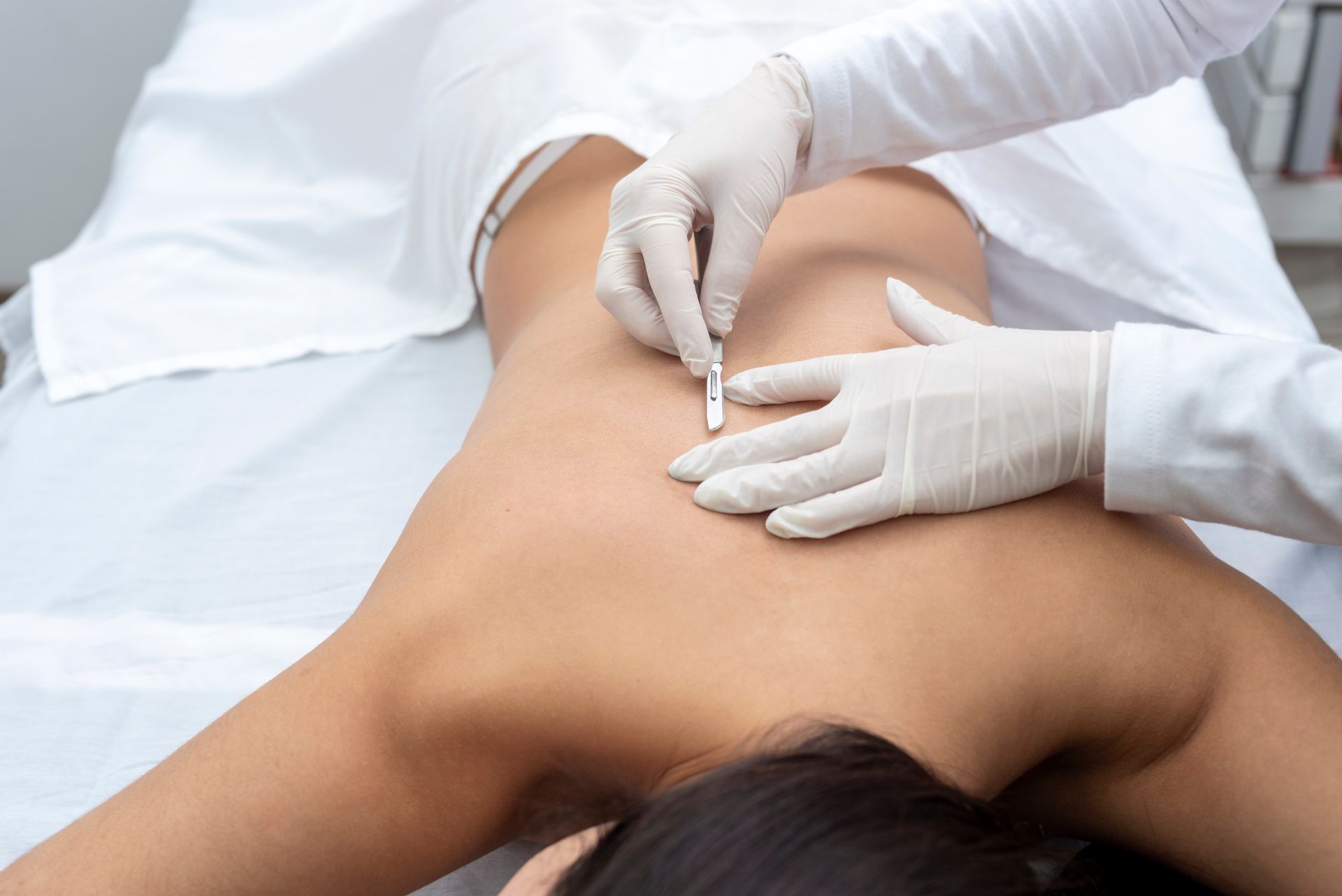 Gloved hands injecting the upper back of a person lying face down on a treatment table