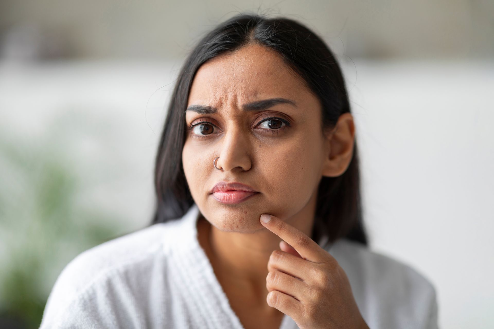 Concerned person in a white robe touching their chin indoors
