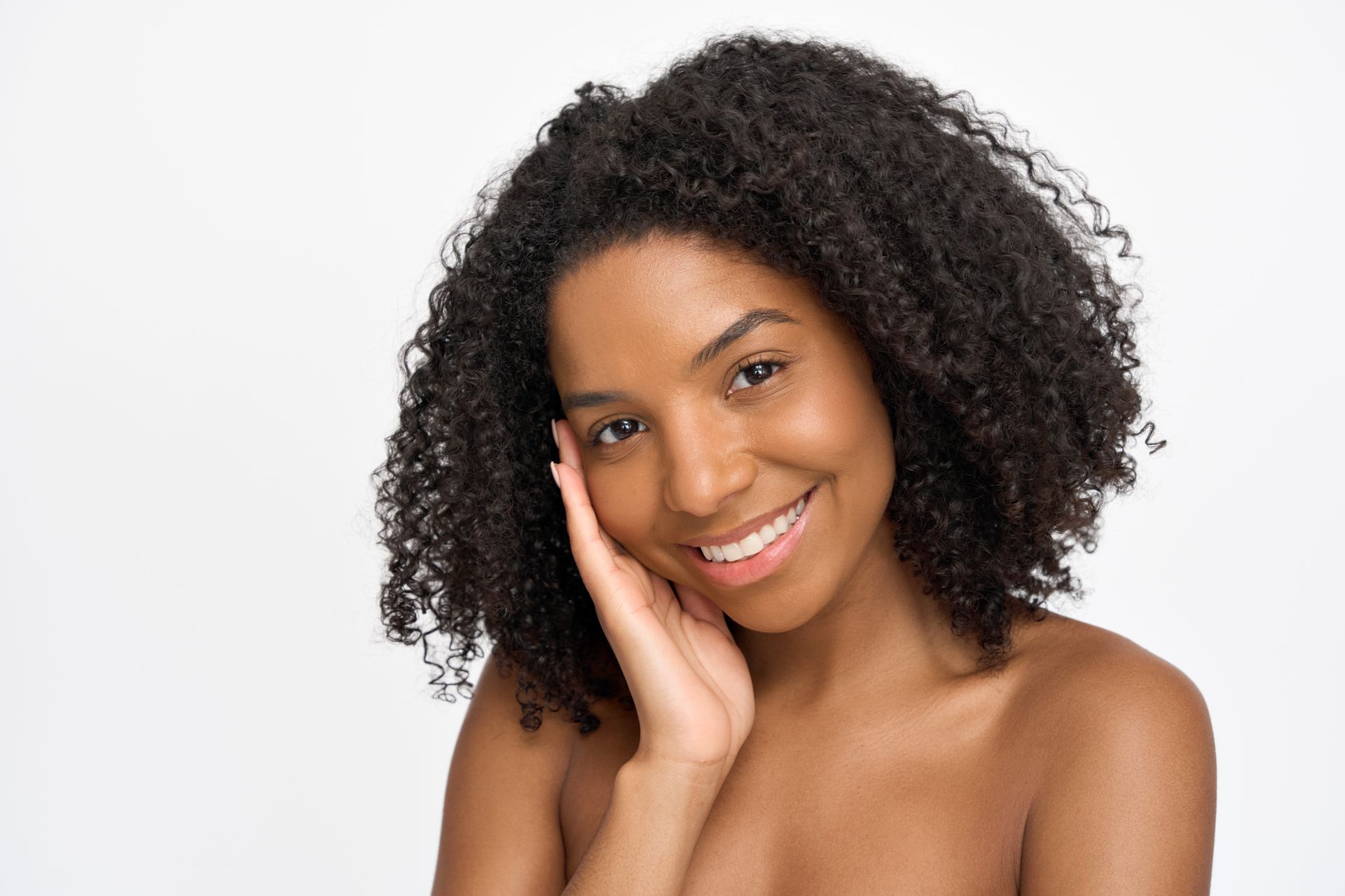Smiling woman with curly hair resting her face on her hand against a white background