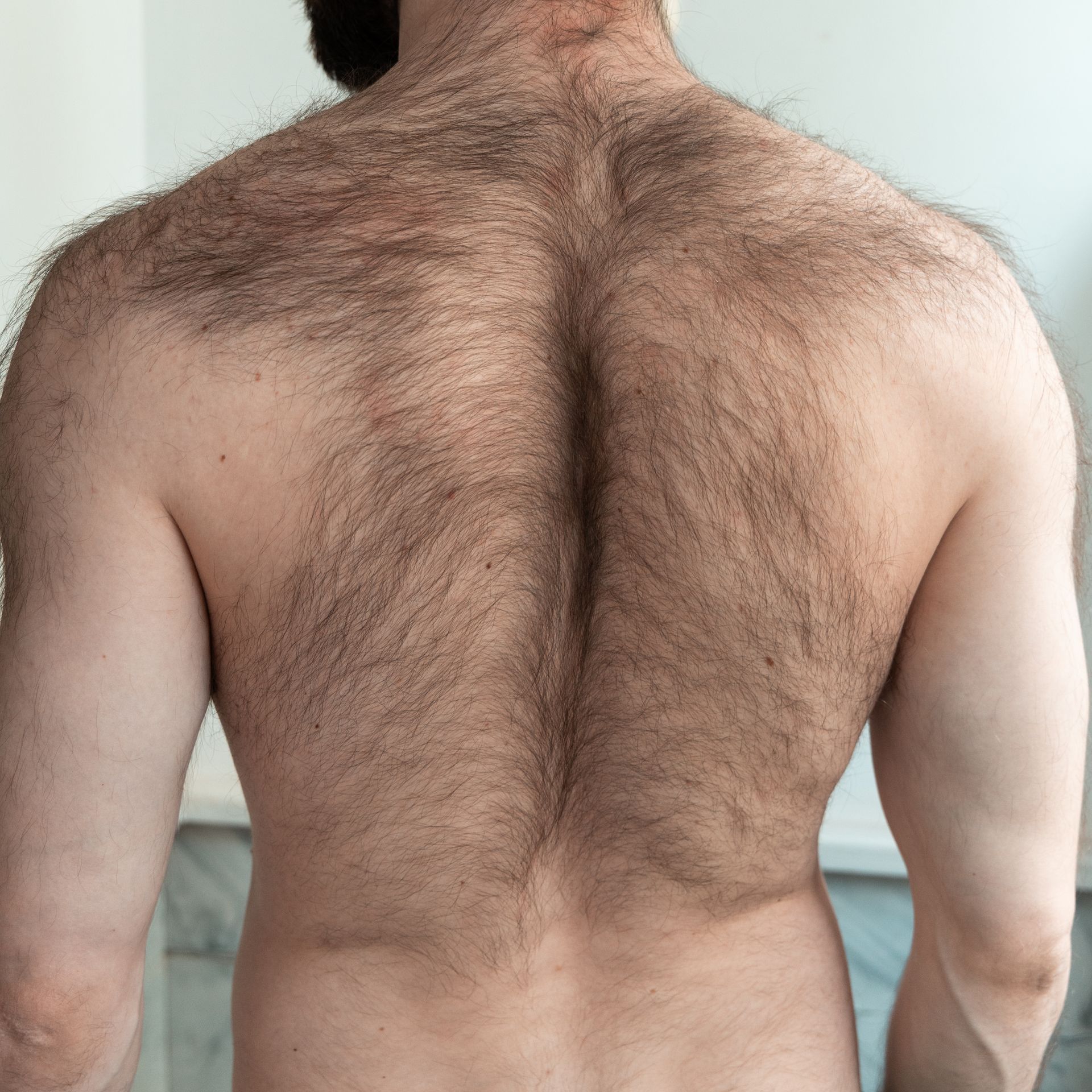 Back of a person with long dark hair and visible back hair, standing indoors