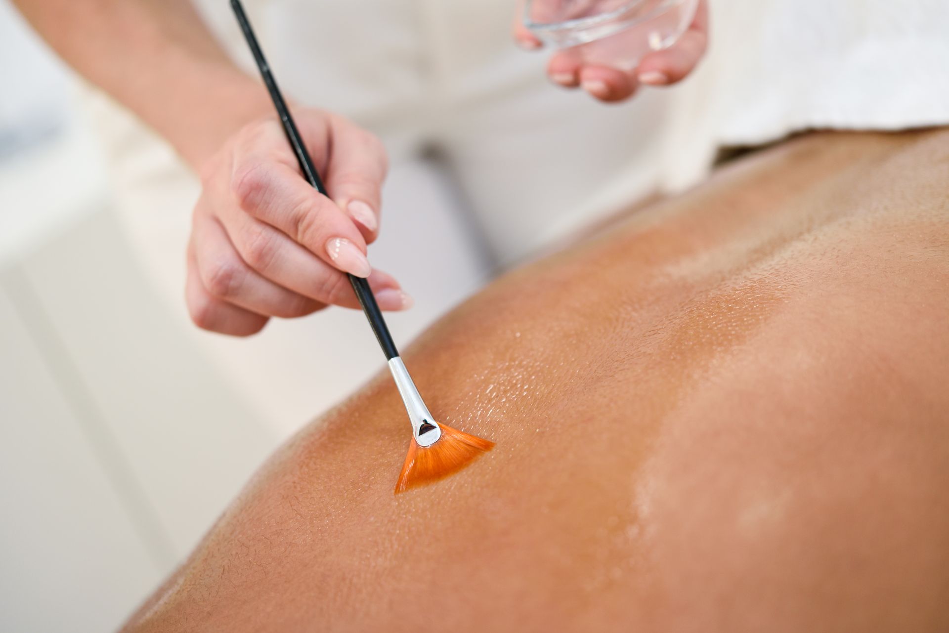 A hand applies orange paste to a person’s back with a brush during a spa treatment.