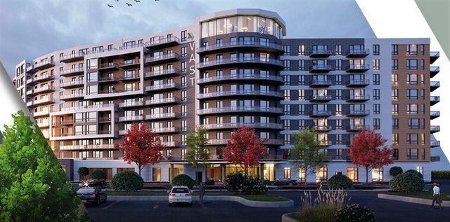 Modern curved apartment building with balconies, large windows, and red trees in front at dusk