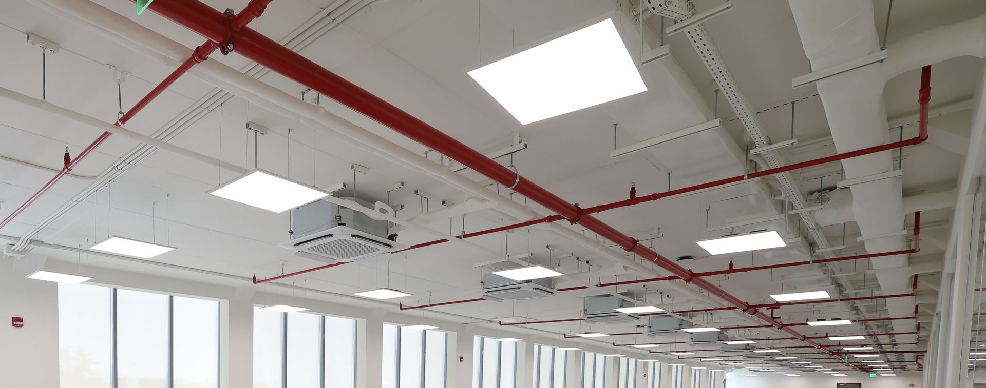 Plafond de bureau vide avec puits de lumière lumineux, tuyaux rouges et grandes fenêtres le long du mur
