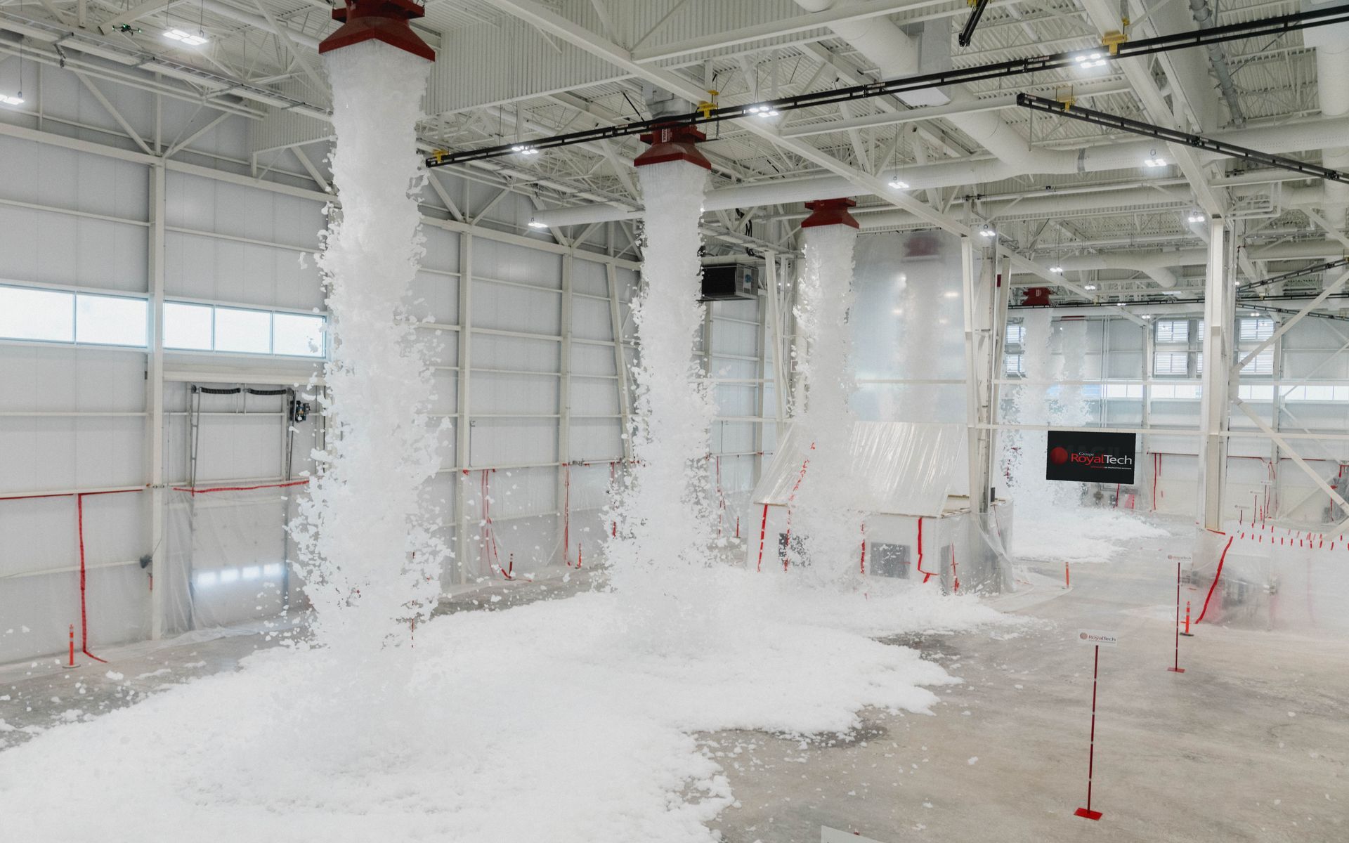 Intérieur industriel recouvert de poussière, avec des colonnes, des tuyaux et un sol recouvert de peinture blanche, dans un espace ressemblant à un entrepôt.
