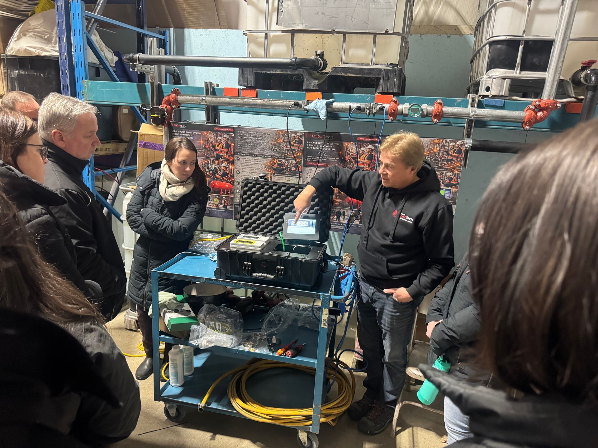 Des personnes étaient rassemblées autour d'une machine dans un atelier industriel, discutant de l'équipement, outils et câbles étant visibles.