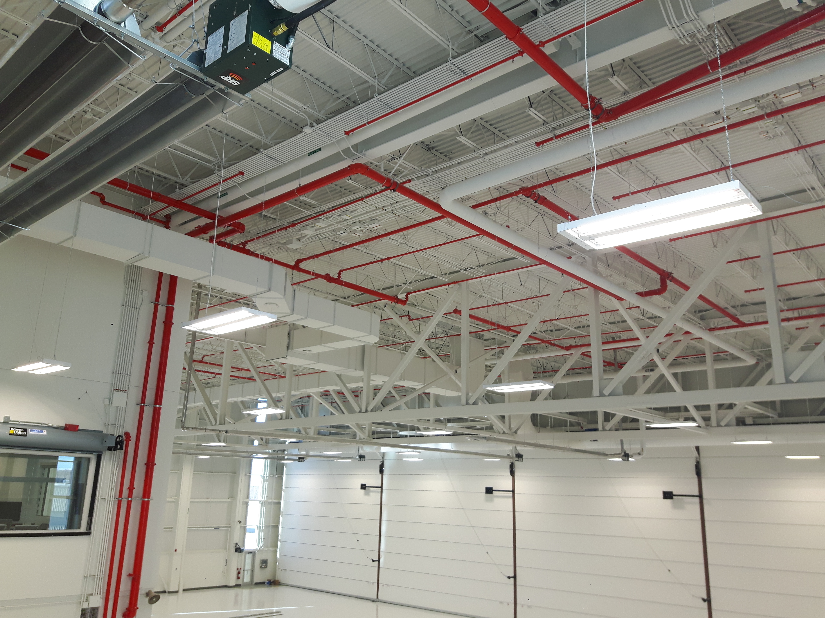 Intérieur de garage industriel avec charpente métallique blanche, tuyaux rouges au plafond et éclairage zénithal vif