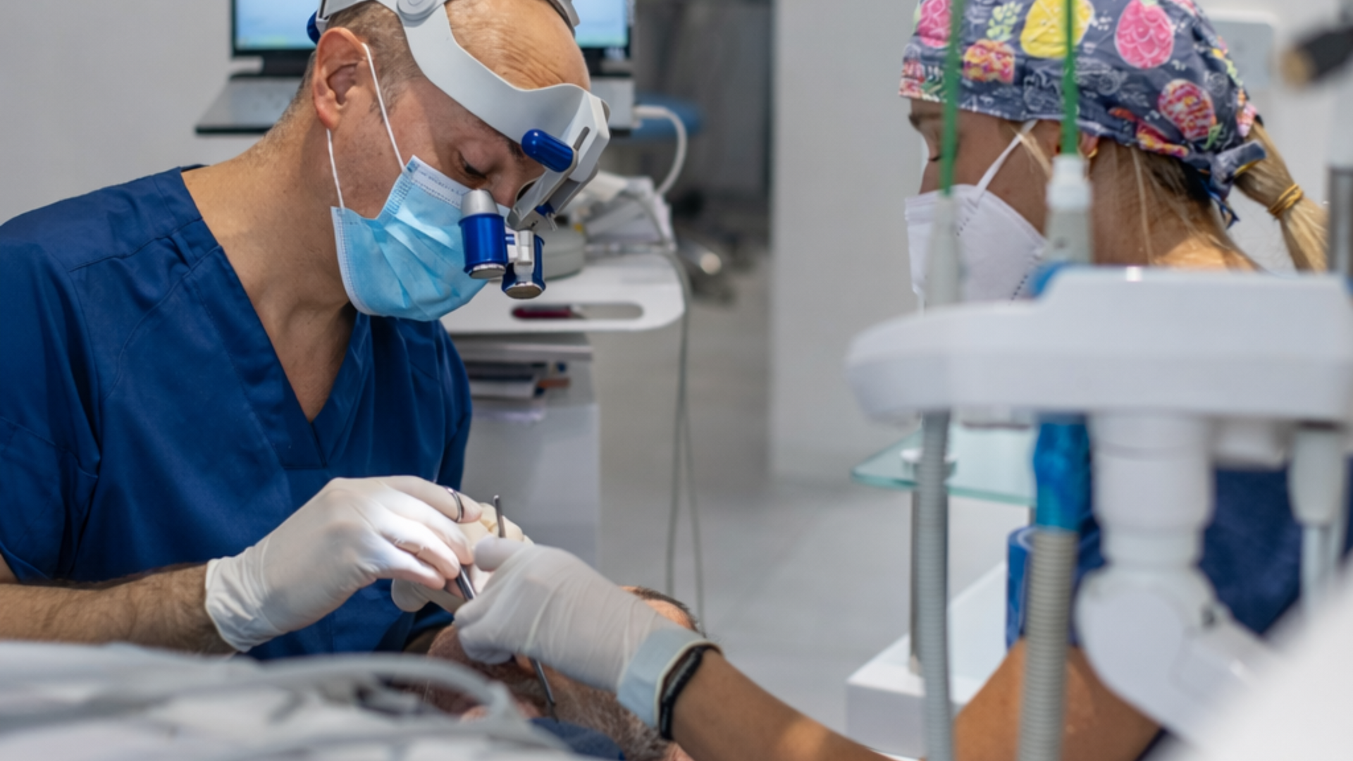 Un dentista con mascherina e visiera protettiva sta lavorando su un paziente in un ambiente clinico.