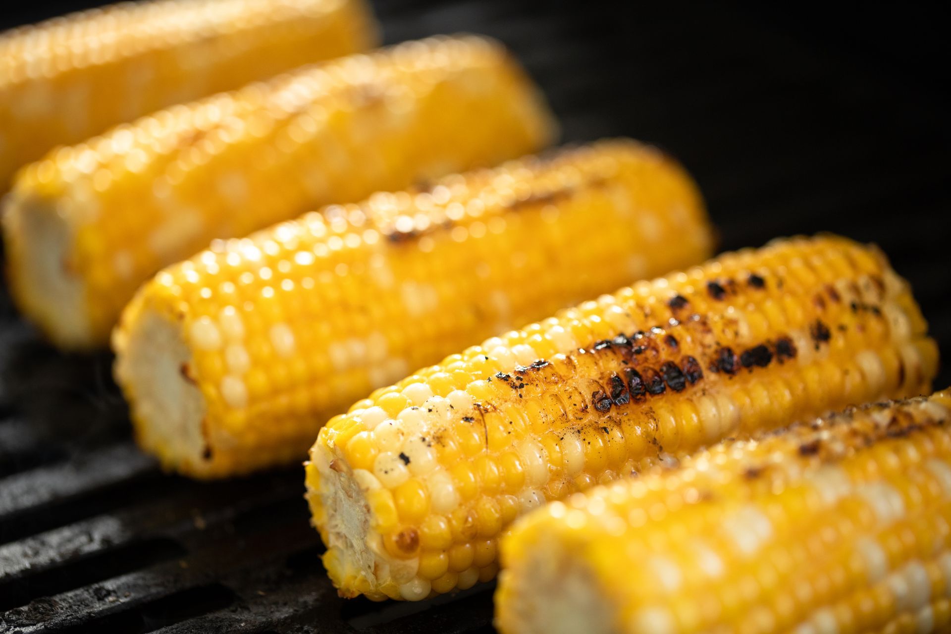Grilled corn on the cob, yellow kernels, with char marks, on a black grill grate. Grilled corn on the cob, yellow kernels, with char marks, on a black grill grate.