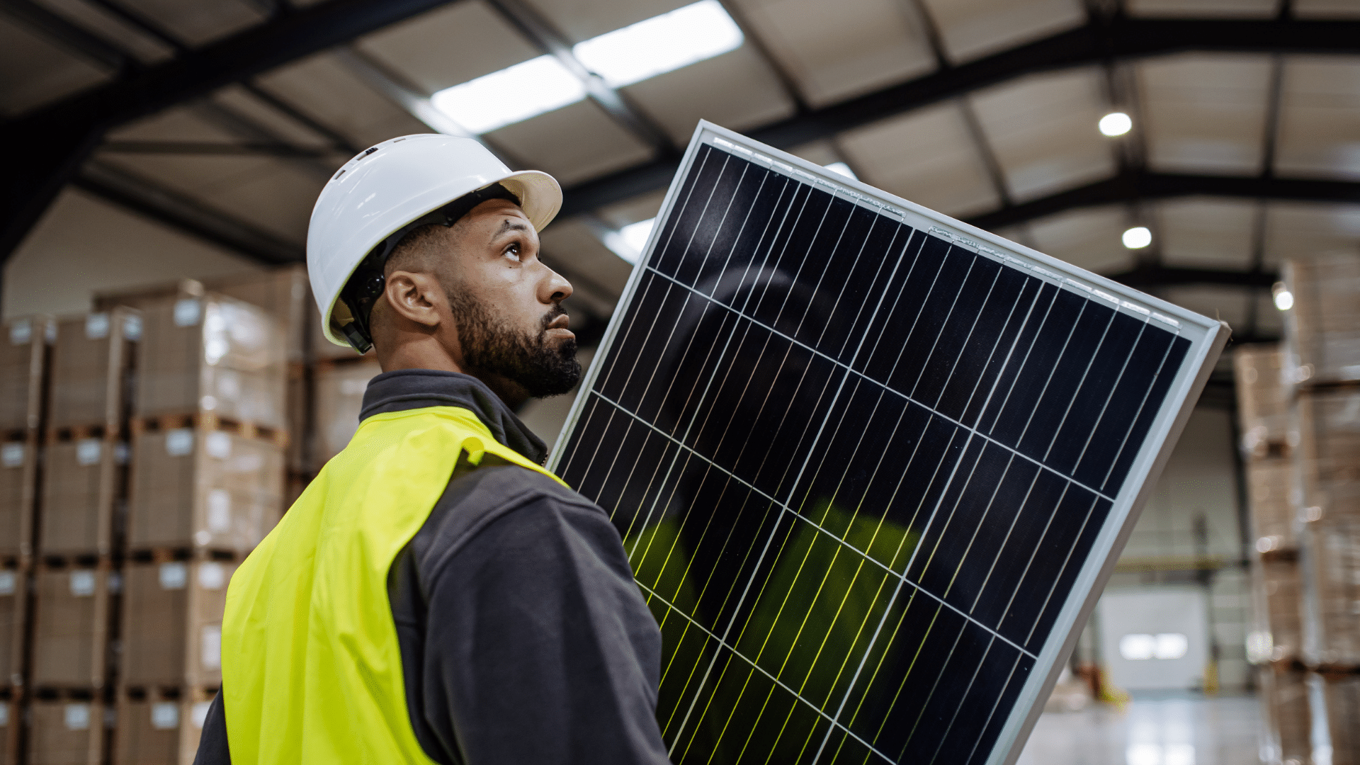 Worker in hard hat carrying a solar panel inside a warehouse