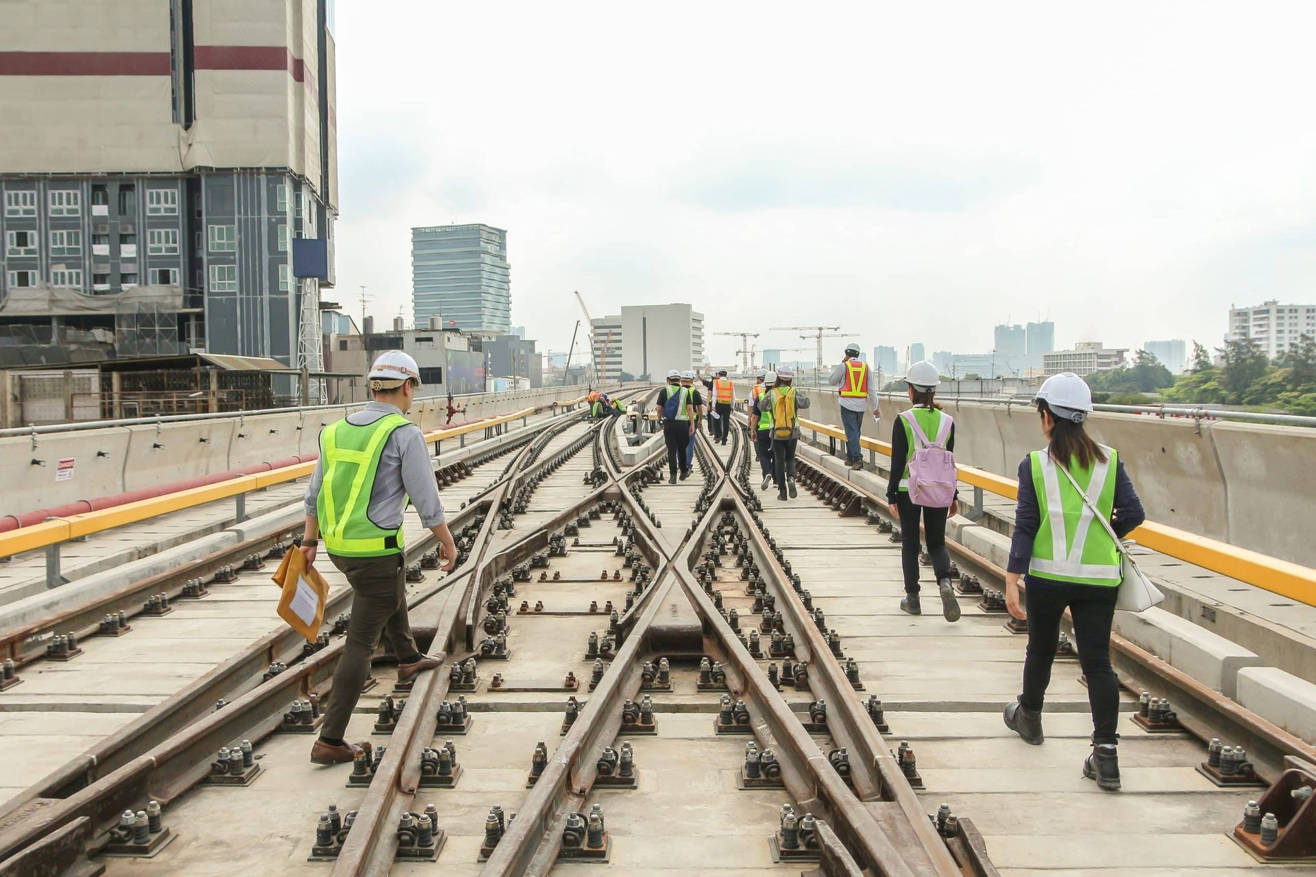 Workers in hard hats and safety vests inspect railway tracks on an elevated bridge under construction.