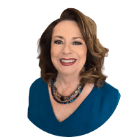 Smiling woman in a blue top with a beaded necklace against a white background