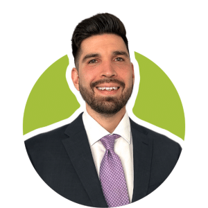 A man with dark hair and a beard, wearing a dark suit and a light purple tie, smiling against a lime green background.