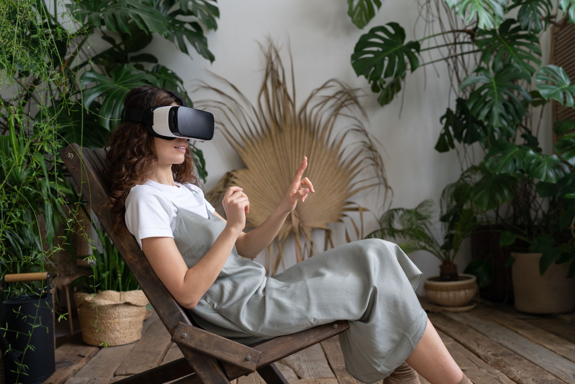 Person lounging in a wooden chair, wearing a VR headset in a lush indoor plant-filled room.