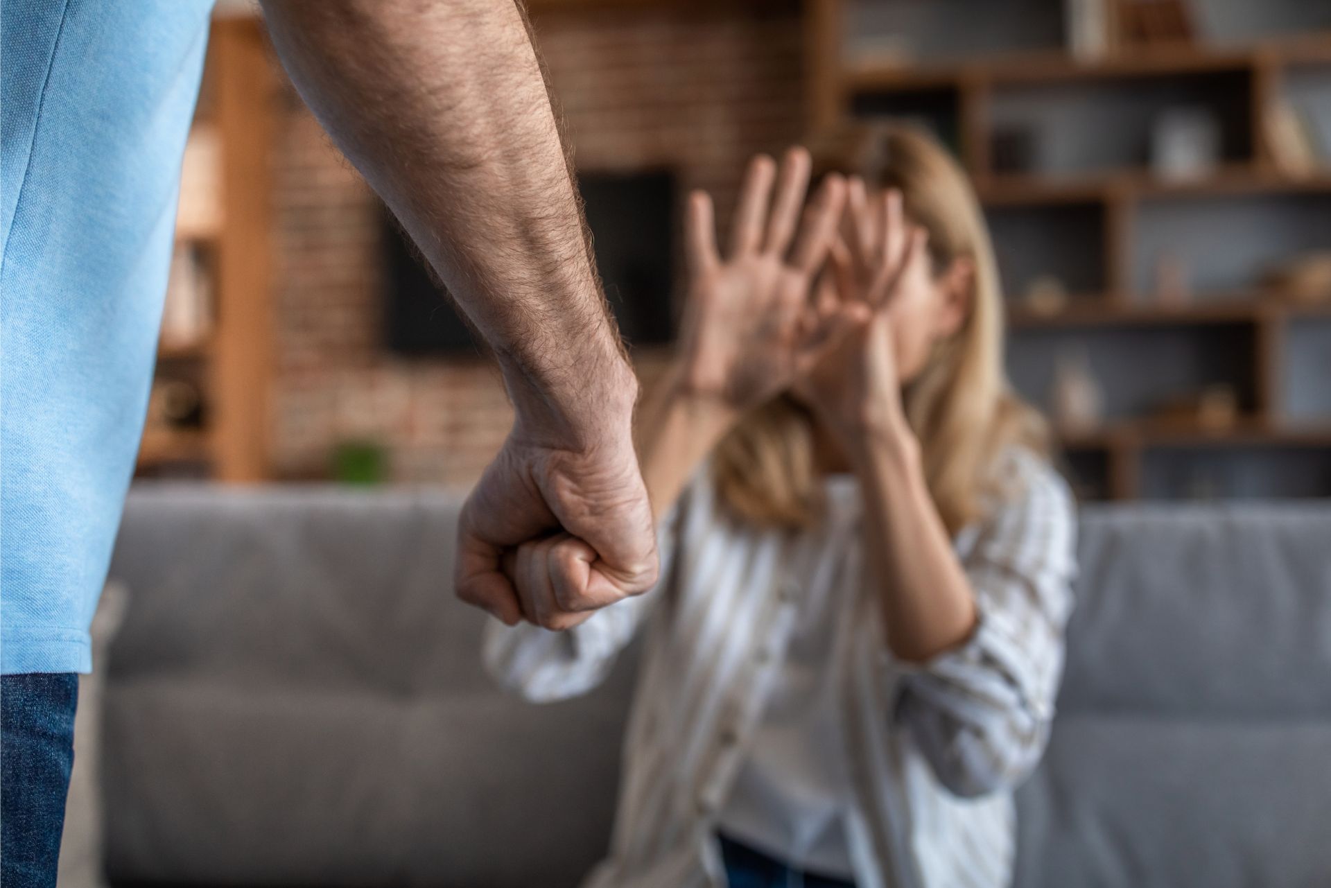 Raised fist in foreground while a seated person covers their face, suggesting an argument indoors.