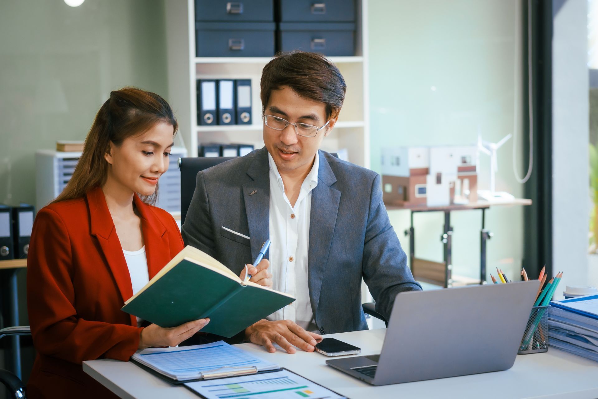 Two coworkers reviewing documents at a desk with a laptop in a modern office