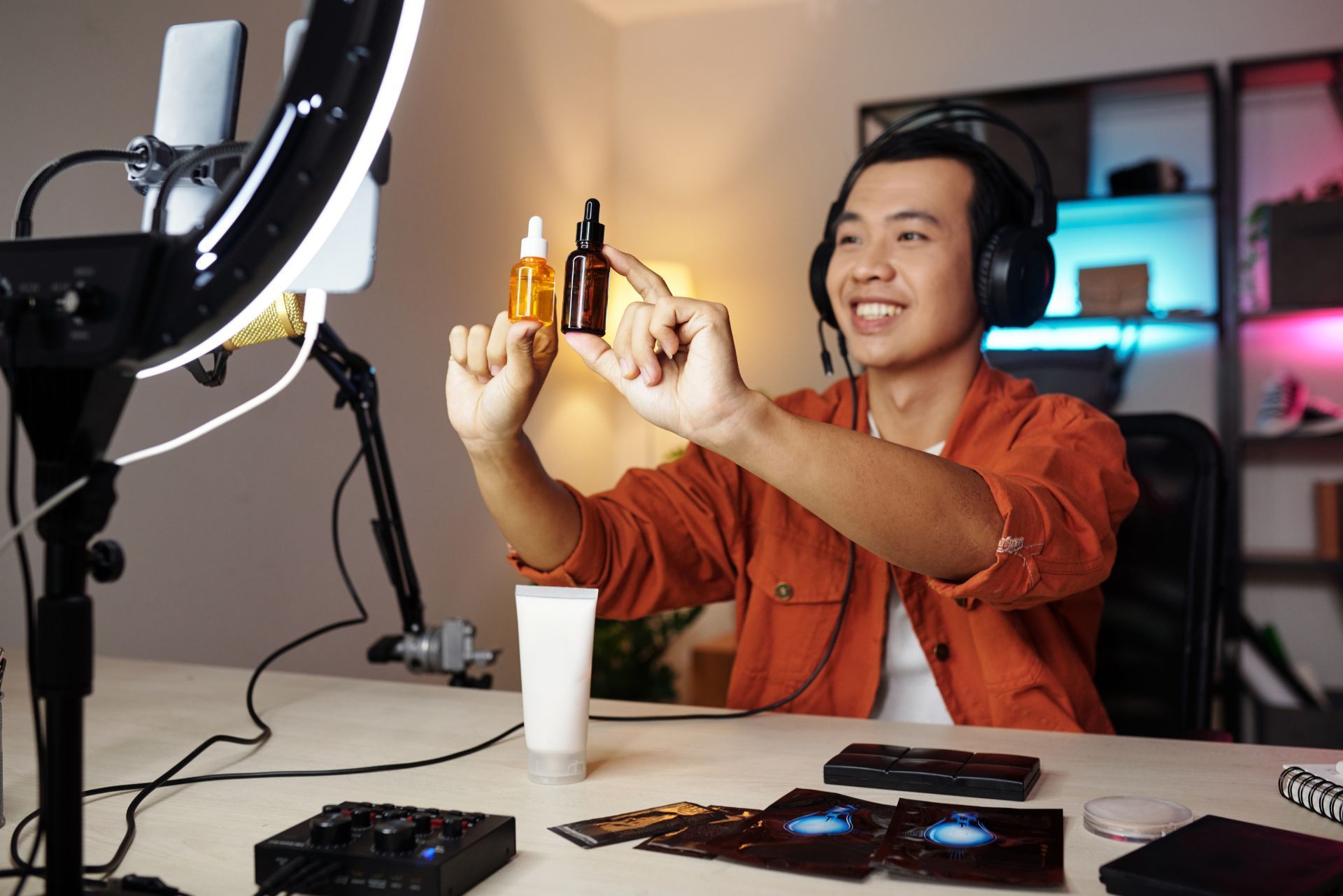 Person wearing headphones recording at a desk with a microphone, camera, and warm studio lights