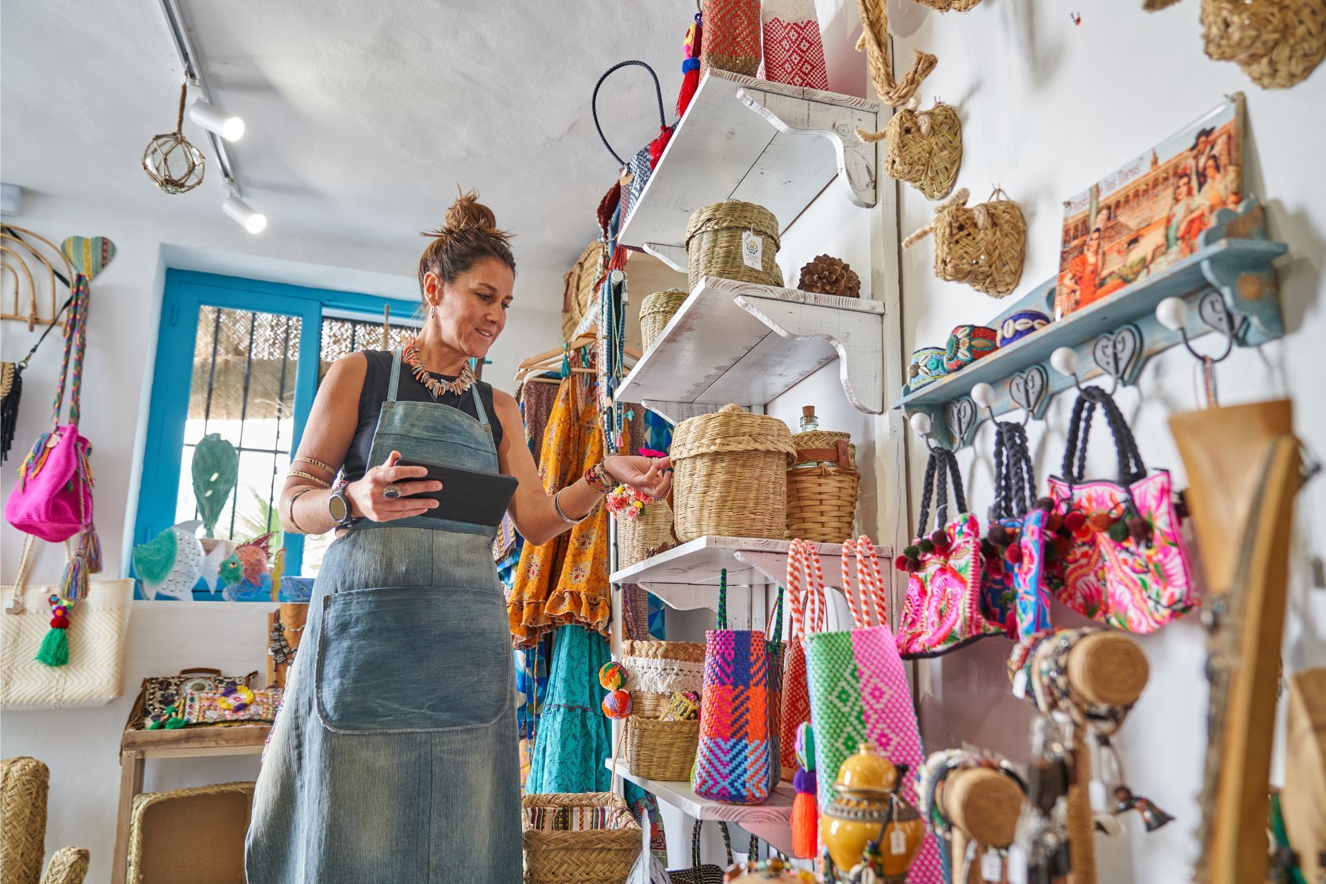 Woman arranging colorful handmade bags in a bright craft shop