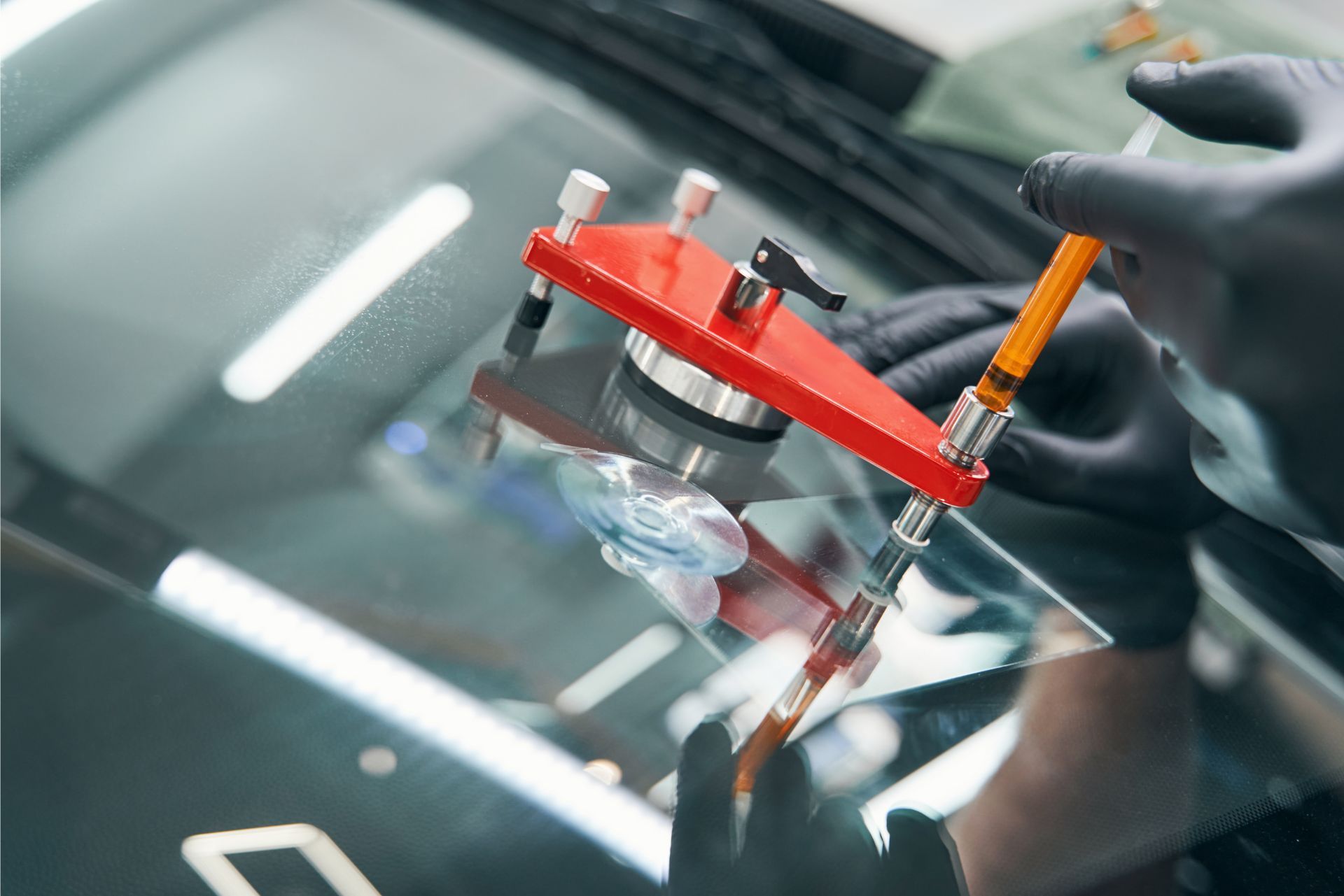 Mechanic using a red windshield repair tool on a car windshield close-up