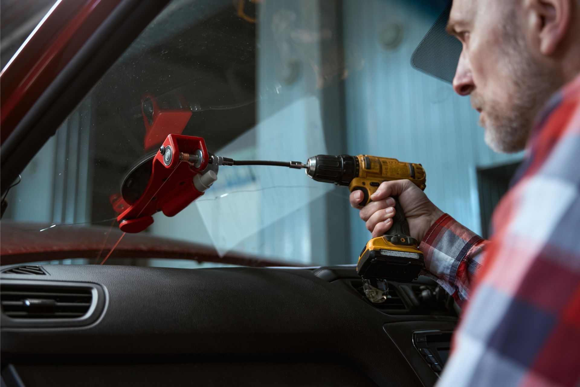 Man using a drill to remove a red side mirror from a car door interior