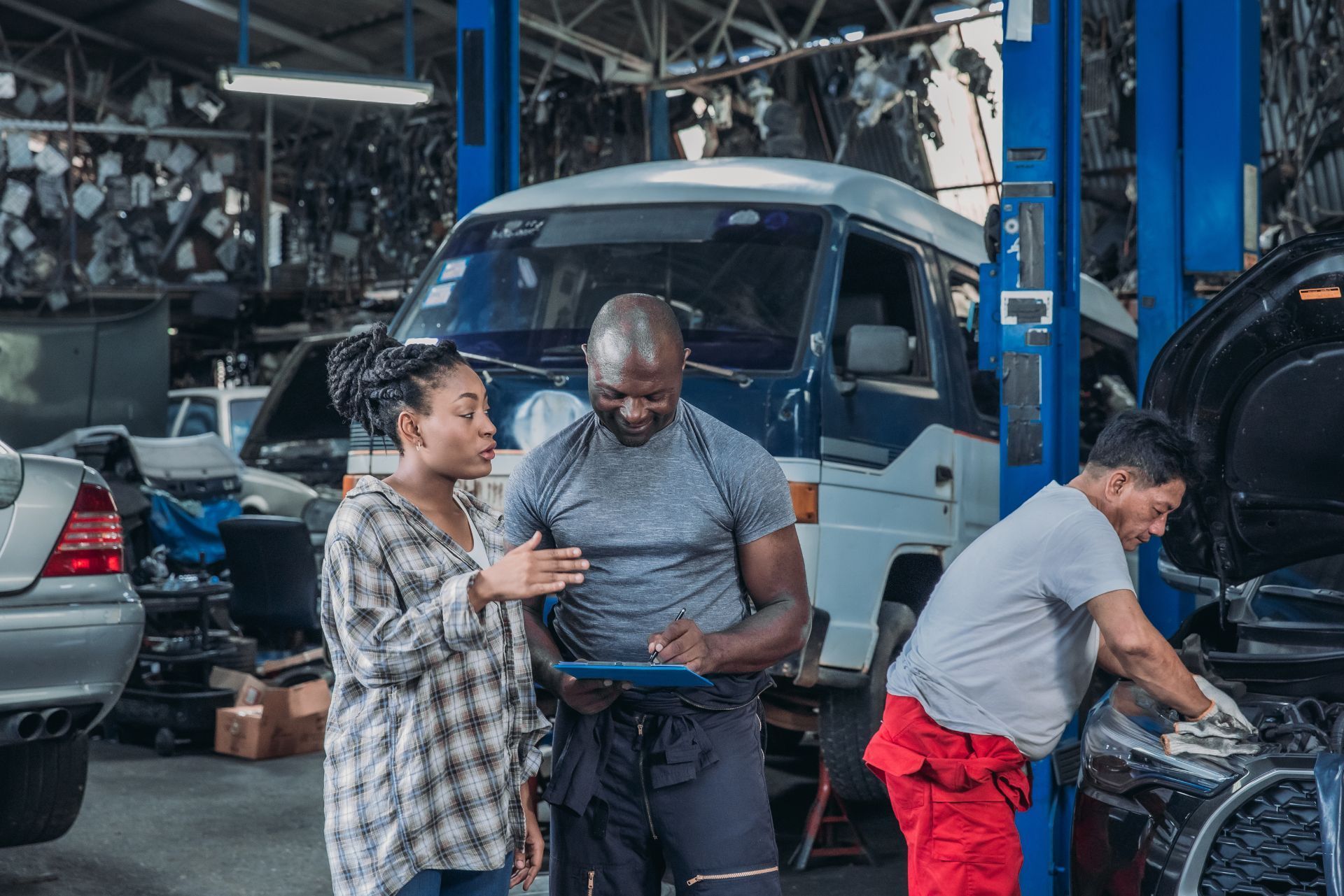 Three people working on a vehicle in a busy auto repair shop