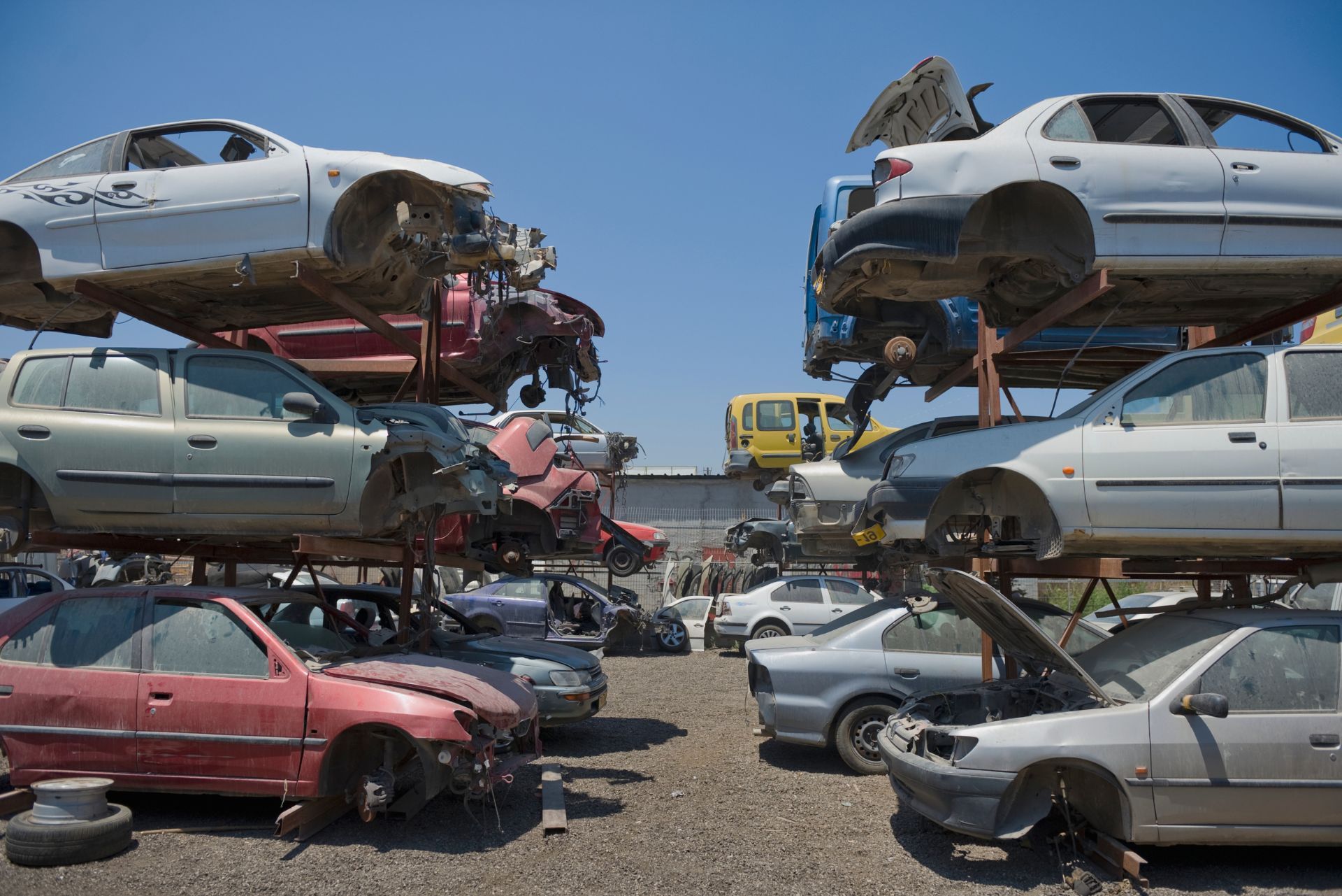 Stacked damaged cars in a scrapyard under a blue sky