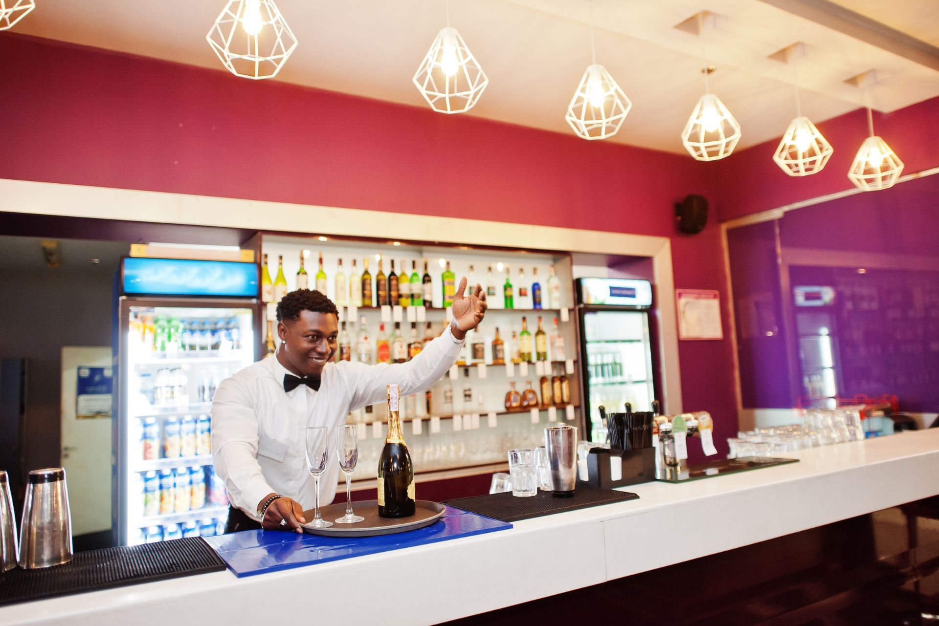 Bartender pouring a drink behind a modern bar with red walls and hanging lights