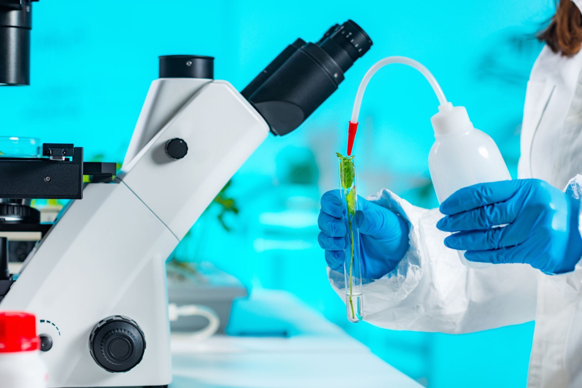 Lab technician holding a sample bottle beside a microscope in a bright laboratory