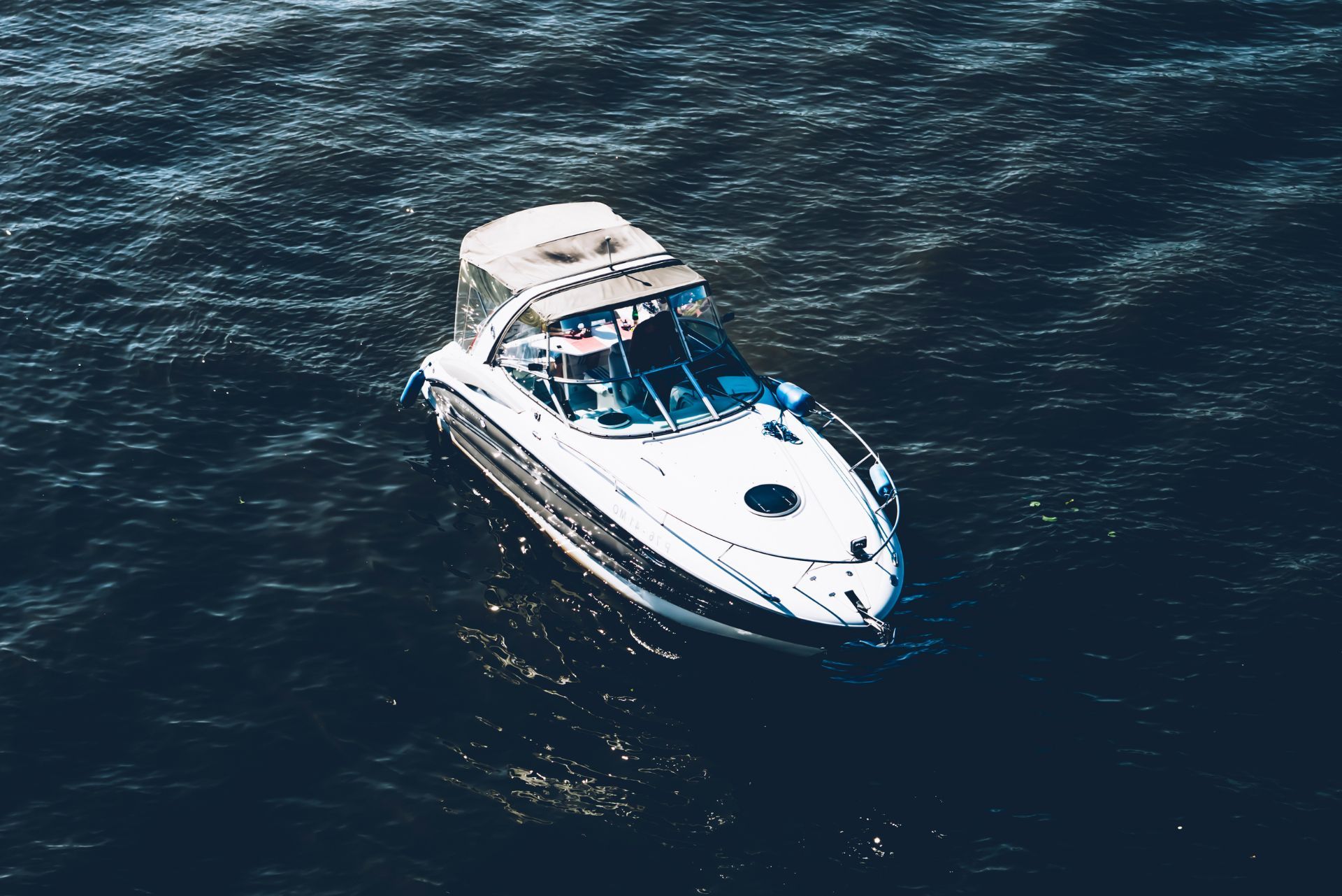 White motor yacht cruising on dark blue ocean water, viewed from above
