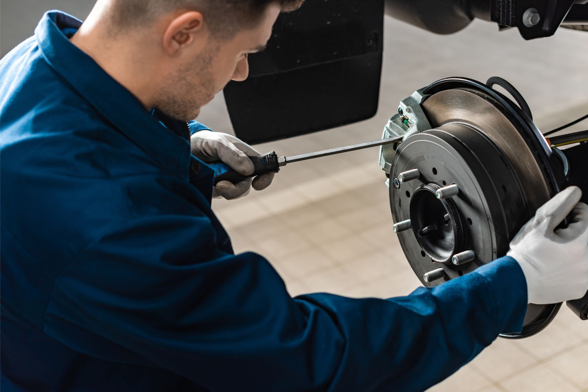 Mechanic in blue coveralls inspecting a car brake disc with a tool in a garage
