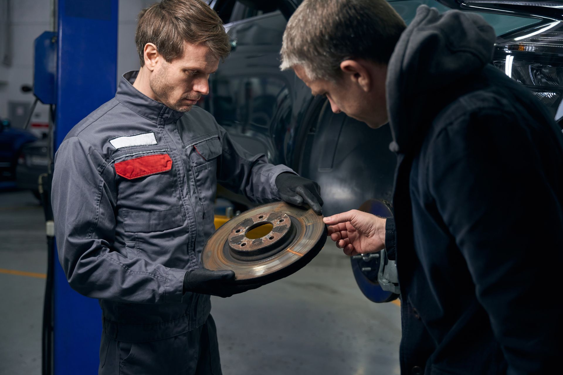 Two mechanics inspecting a car brake rotor in a workshop