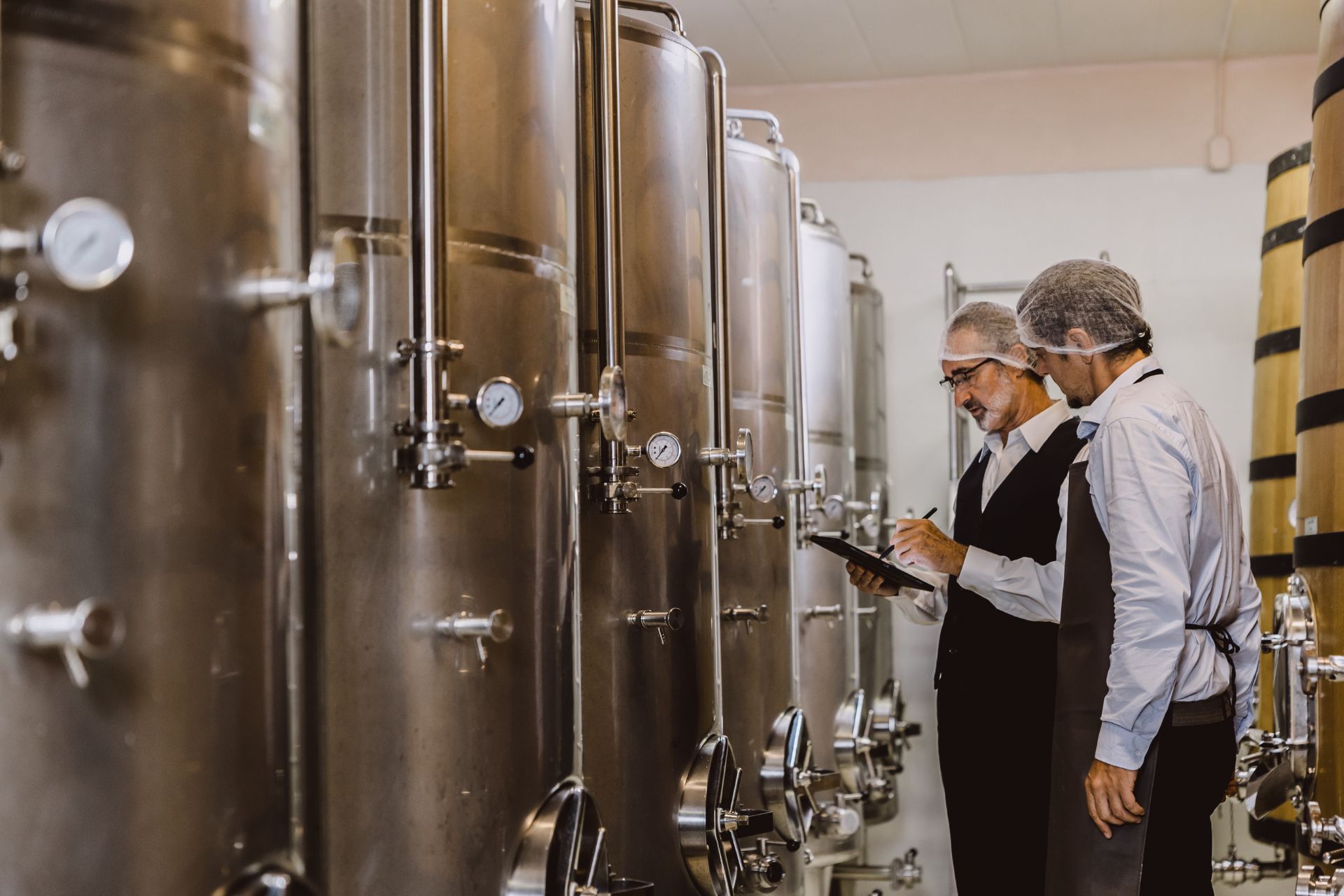 Workers inspecting stainless steel tanks in a brewery cellar