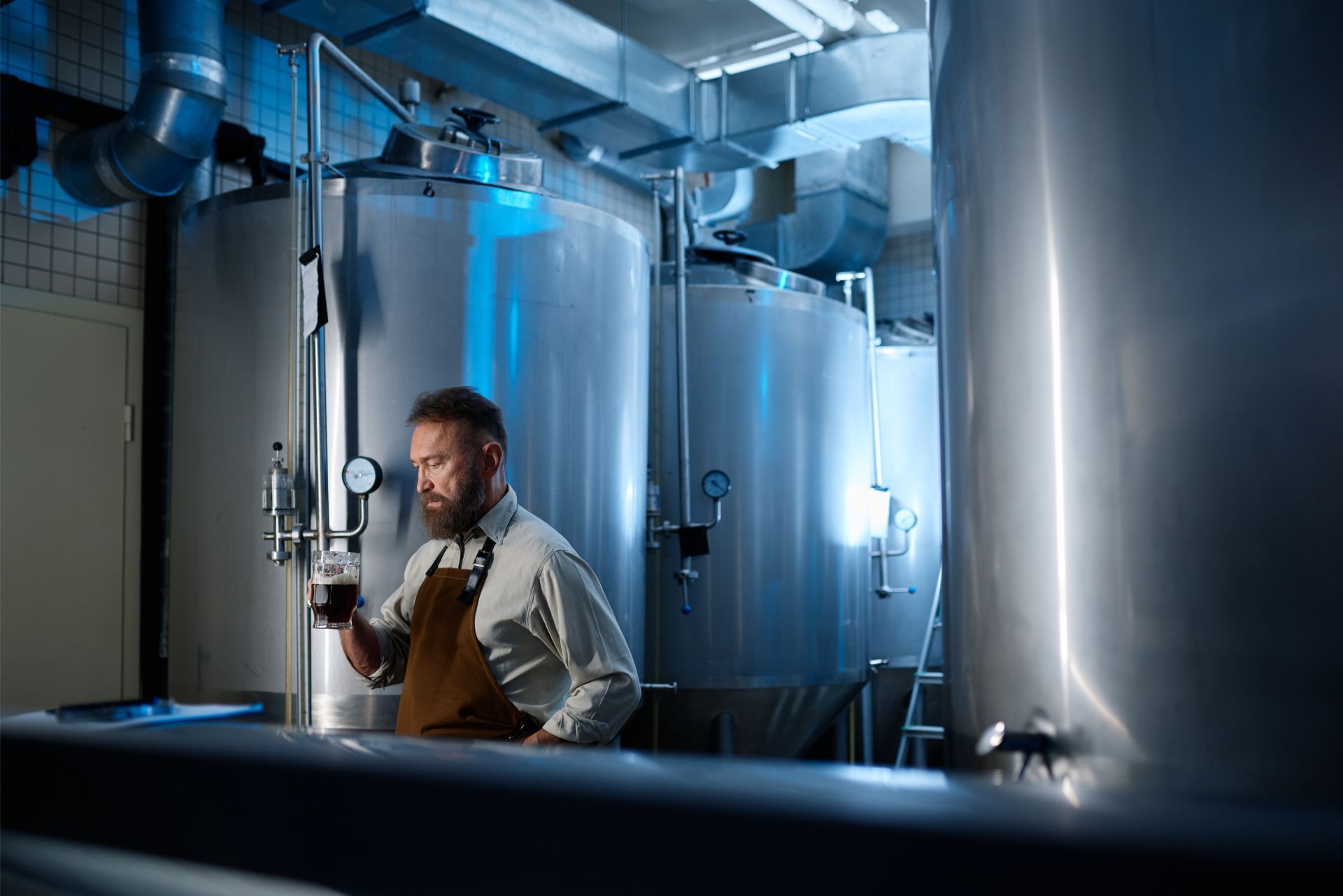 Worker inspecting tanks in an industrial facility, with blue lighting and stainless steel equipment.