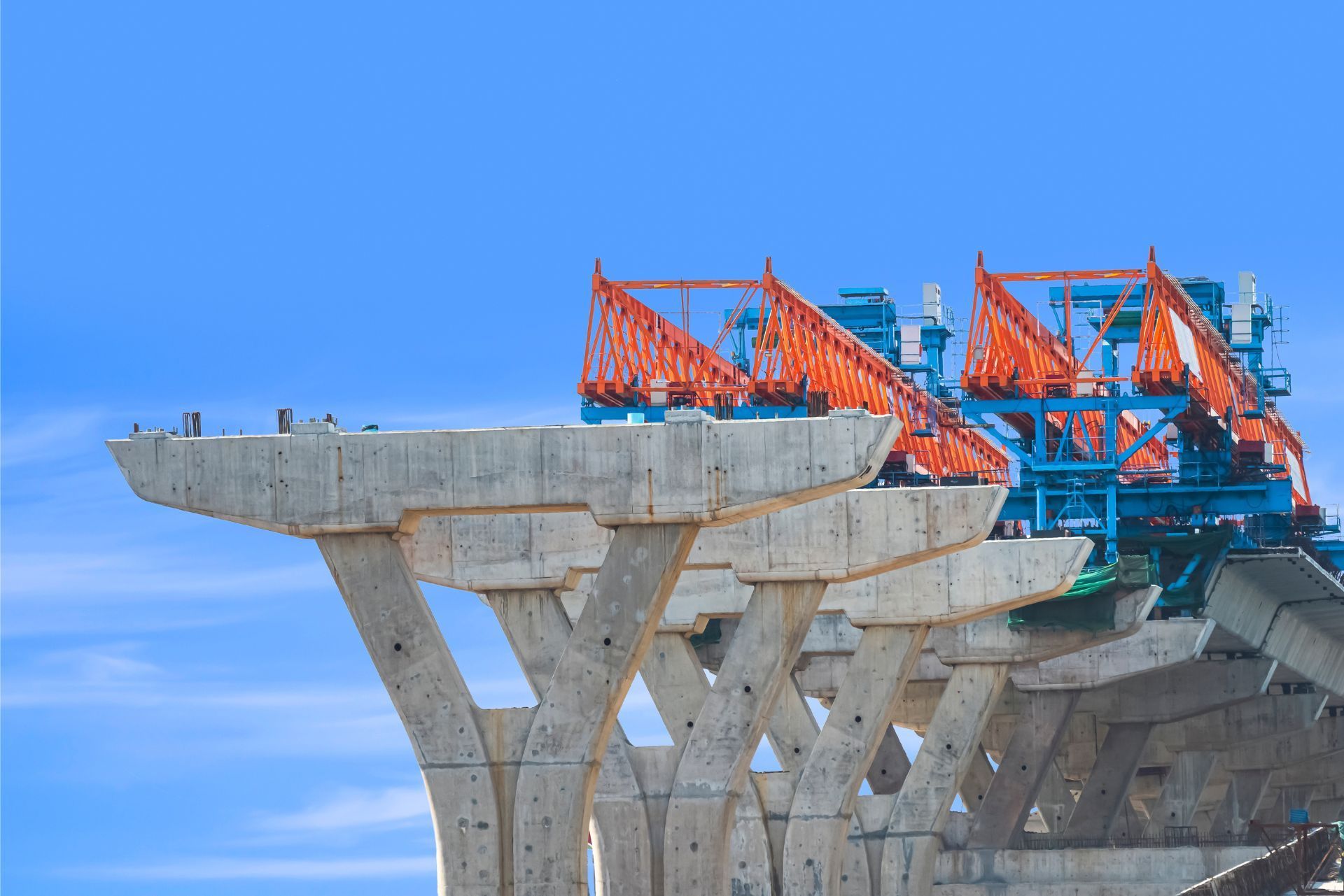 Concrete bridge under construction with red cranes and scaffolding against a blue sky