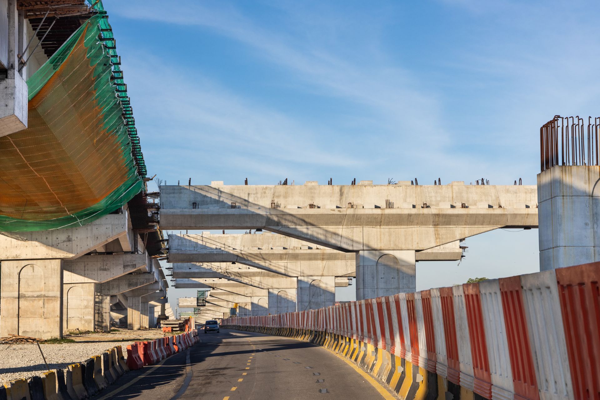 Road under construction with concrete overpass, red-and-white barriers, and blue sky