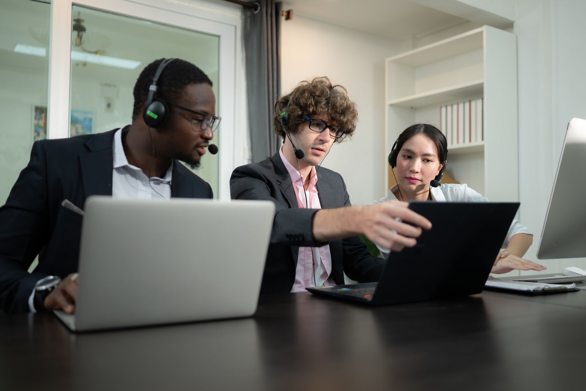 Three coworkers in a meeting, looking at a laptop and discussing something in an office.