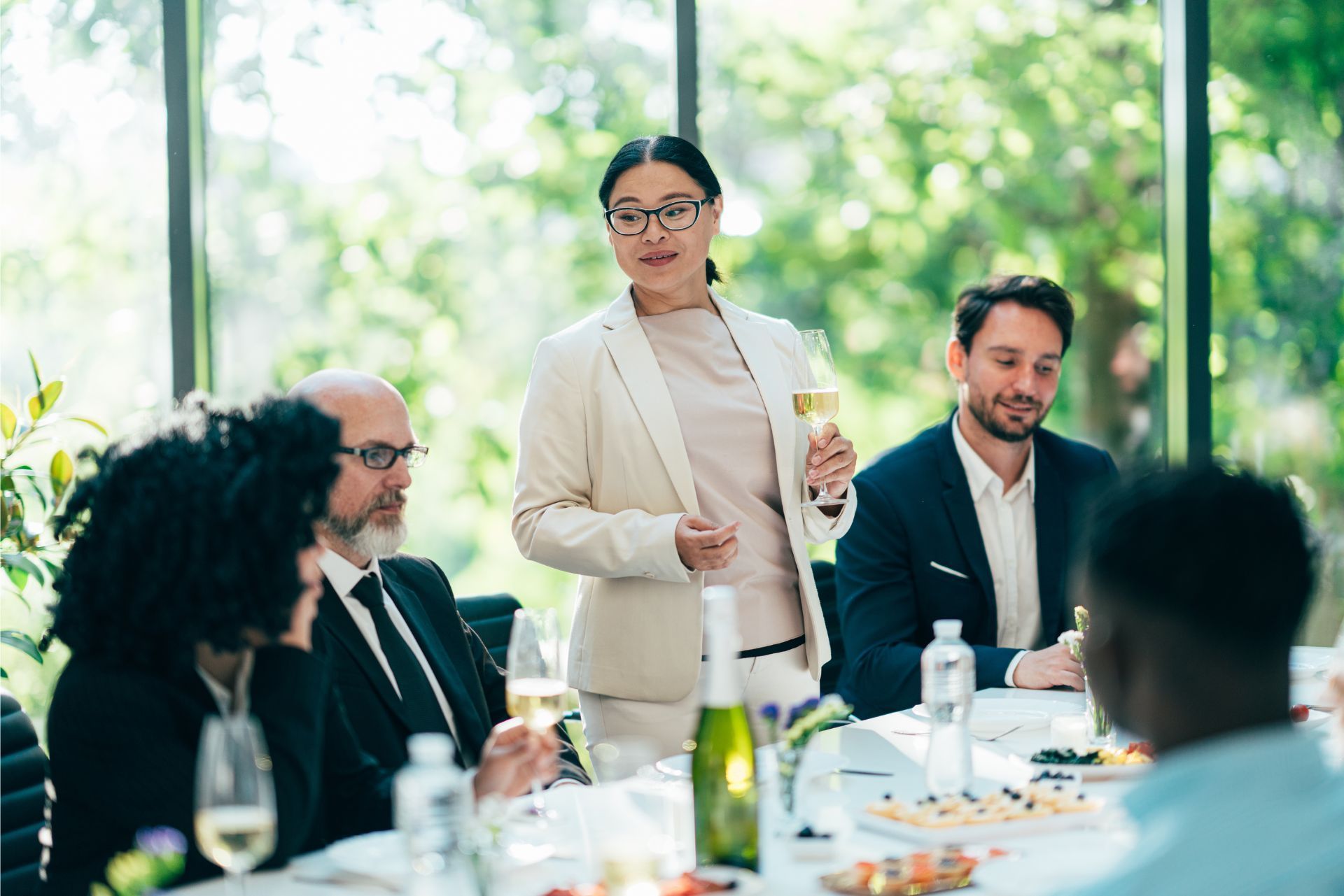 Person speaking at a formal outdoor meeting with seated attendees around a table