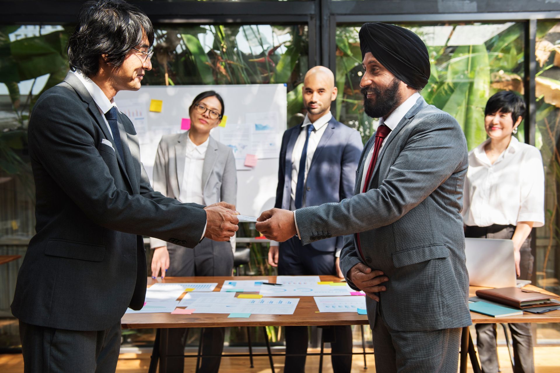 Two business professionals shake hands in a modern office with three colleagues standing in the background.