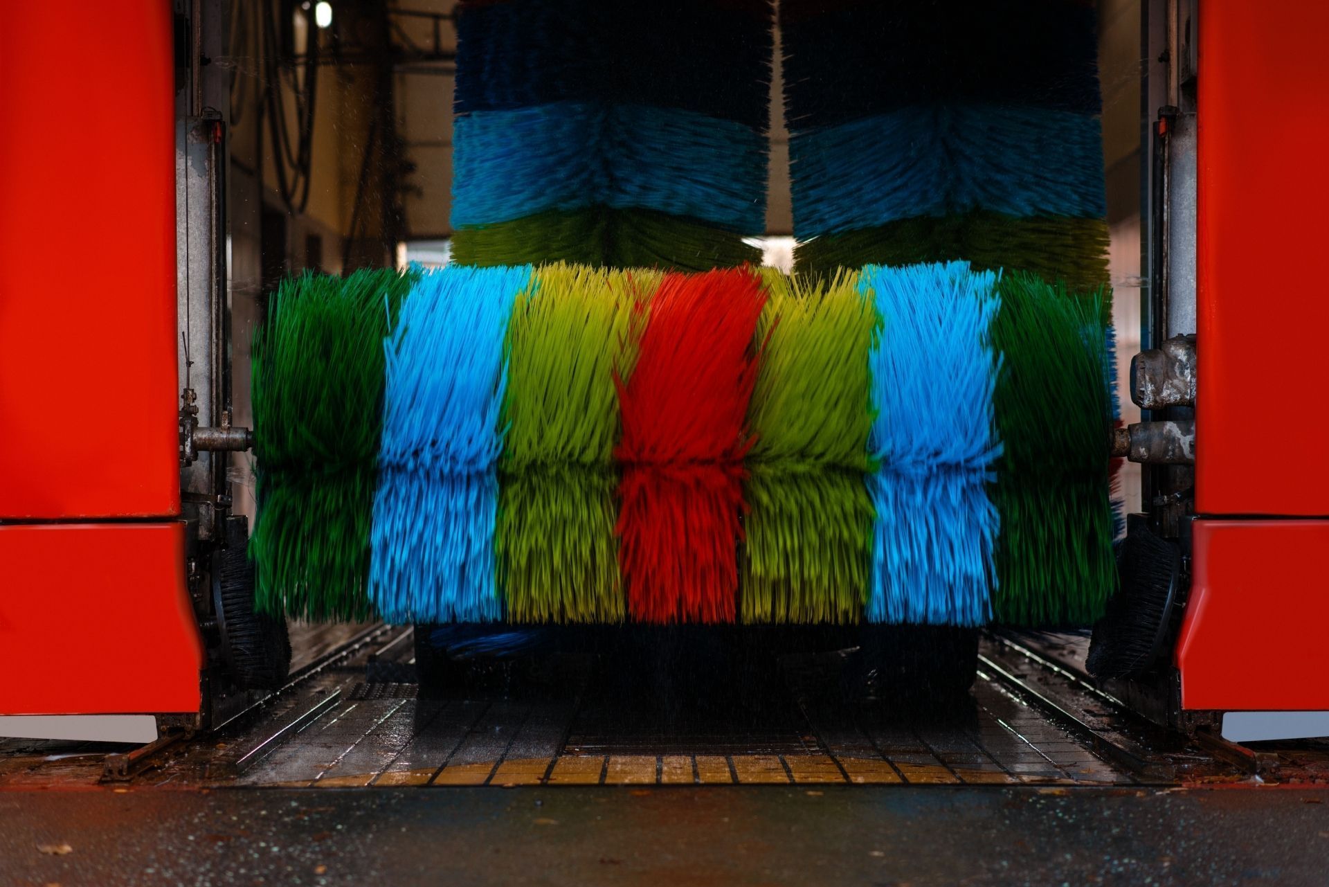 A horizontal, multicolored car wash brush with stripes of green, blue, yellow, and red, positioned between red walls.