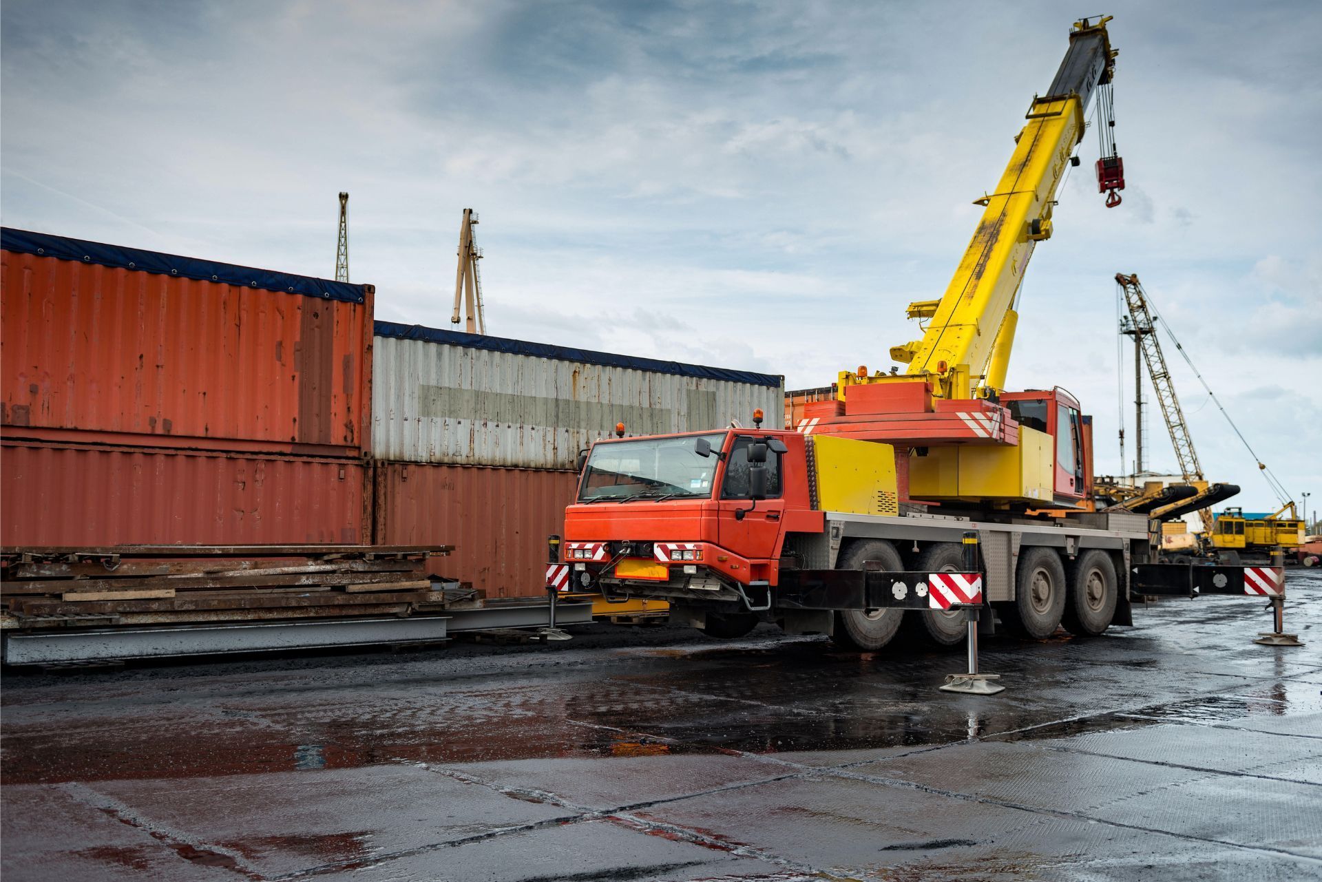 Orange crane truck lifting a load at a shipping yard beside stacked containers