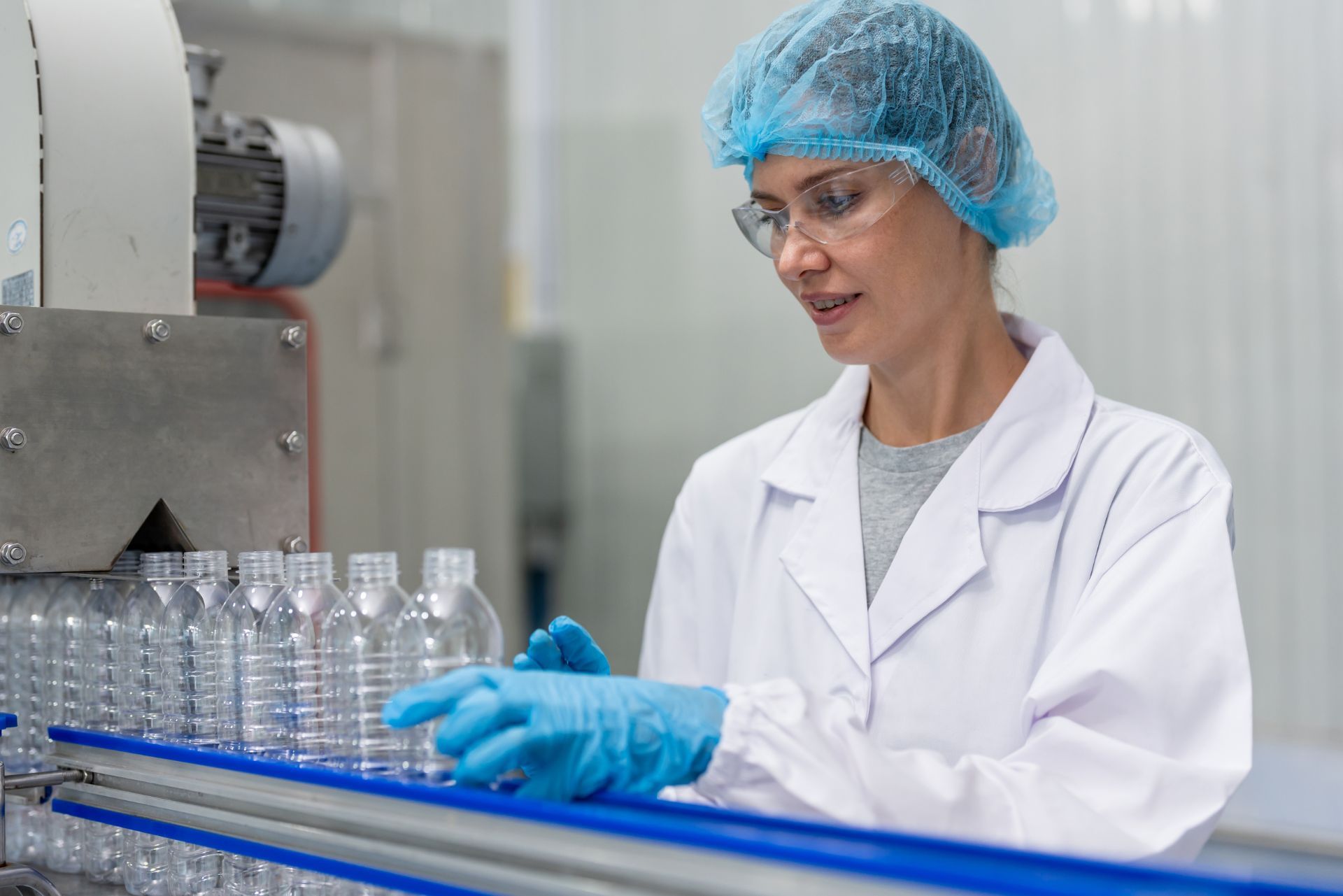 Lab technician in protective gear inspecting bottles on a production line