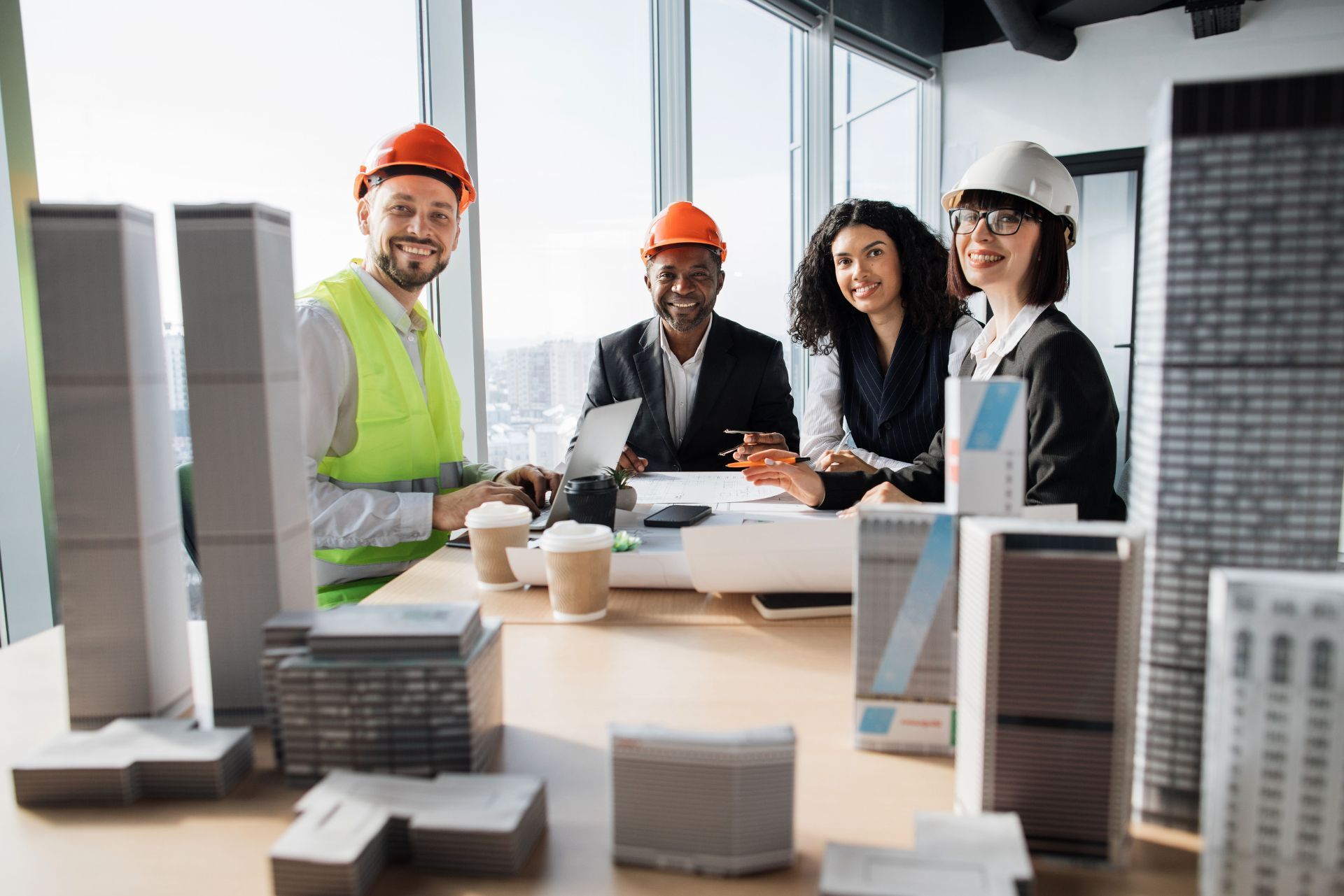 Team in hard hats reviewing building models and plans at a construction meeting table