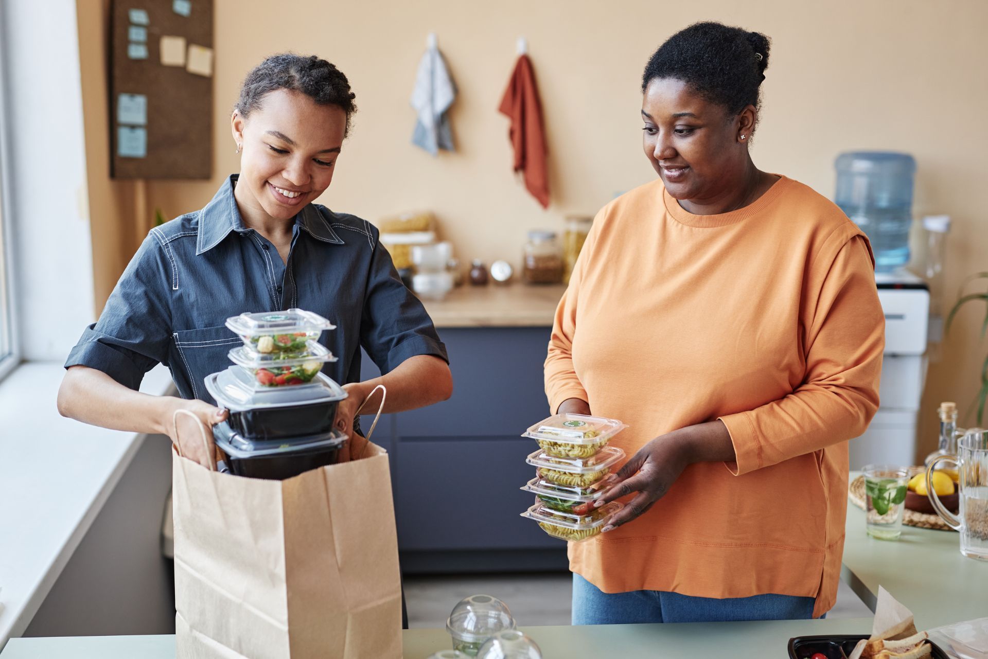 Two people unpacking stacked food containers in a kitchen