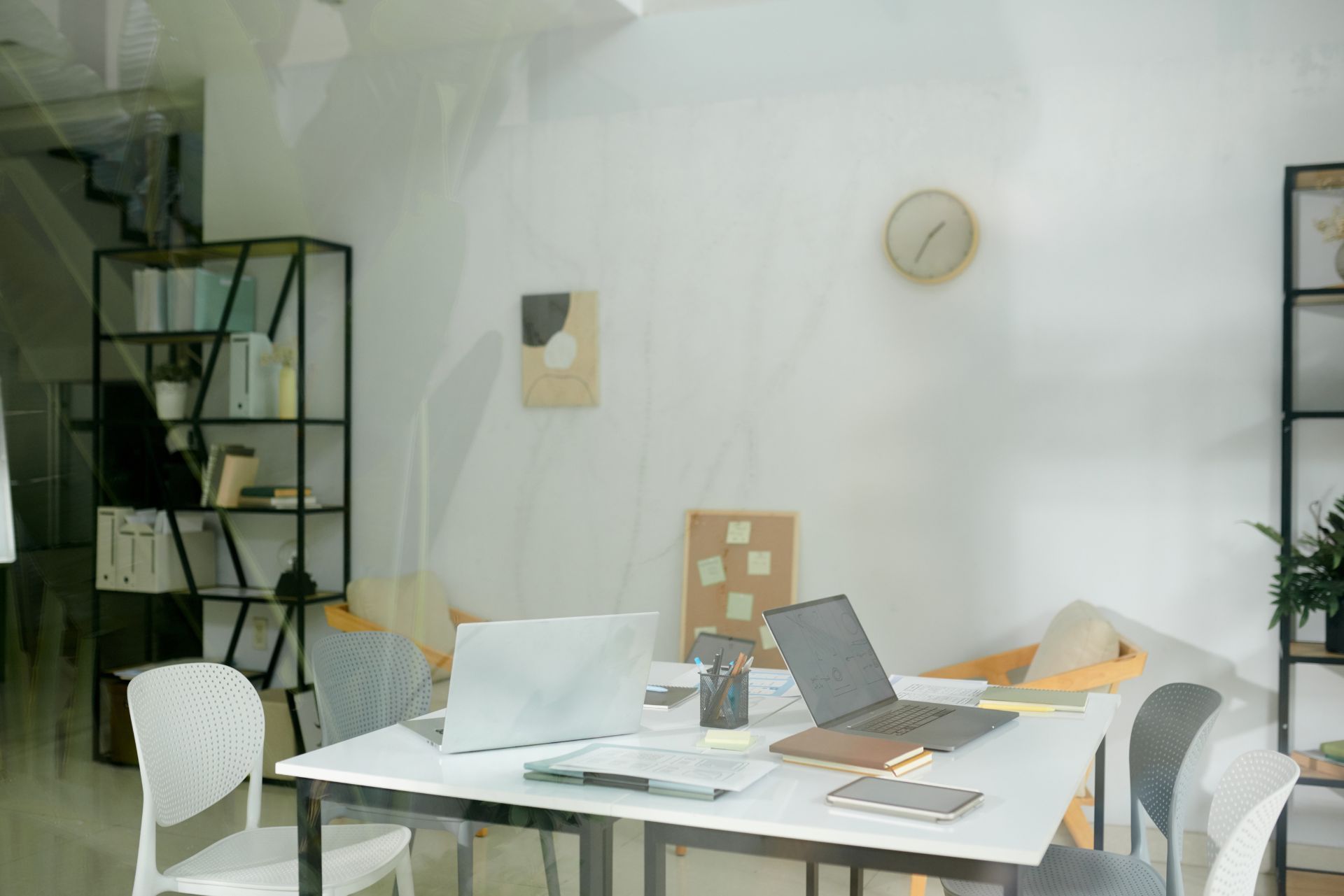 Minimalist office with white desk, open laptops, chairs, shelves, and a wall clock