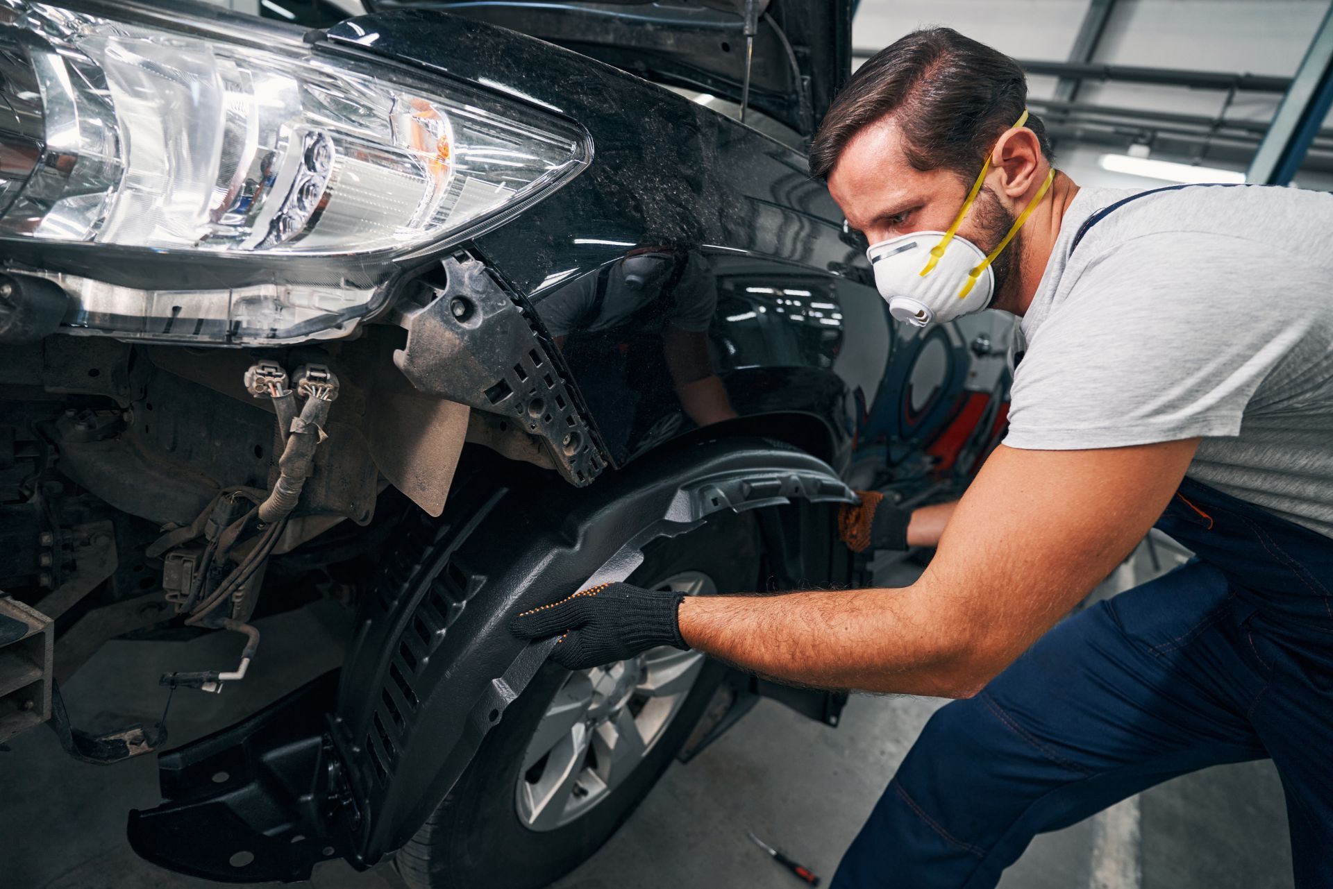 Mechanic in a mask repairing the front wheel of a damaged car in a garage