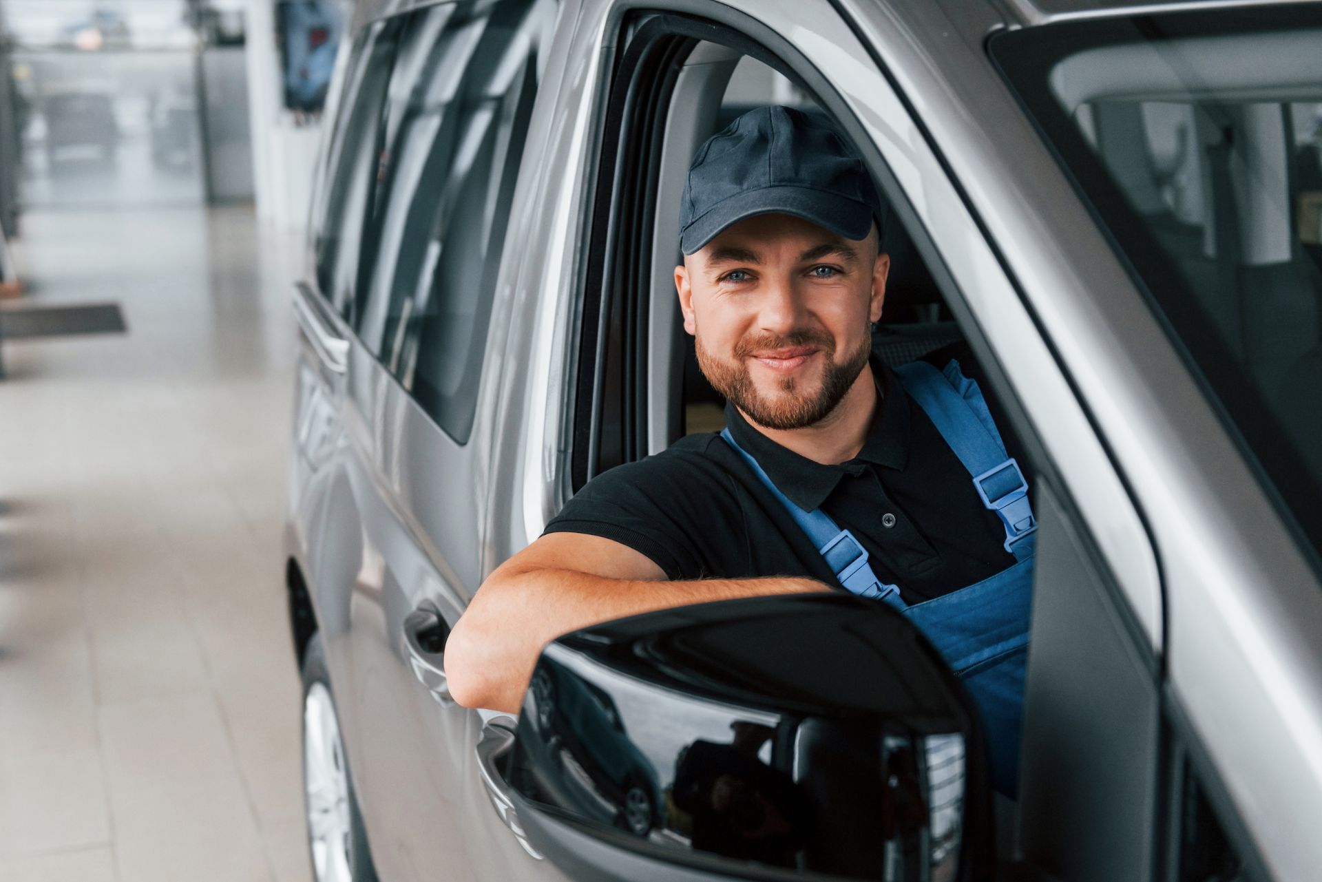 Man smiling in a black cap, leaning out of a silver car window in a showroom
