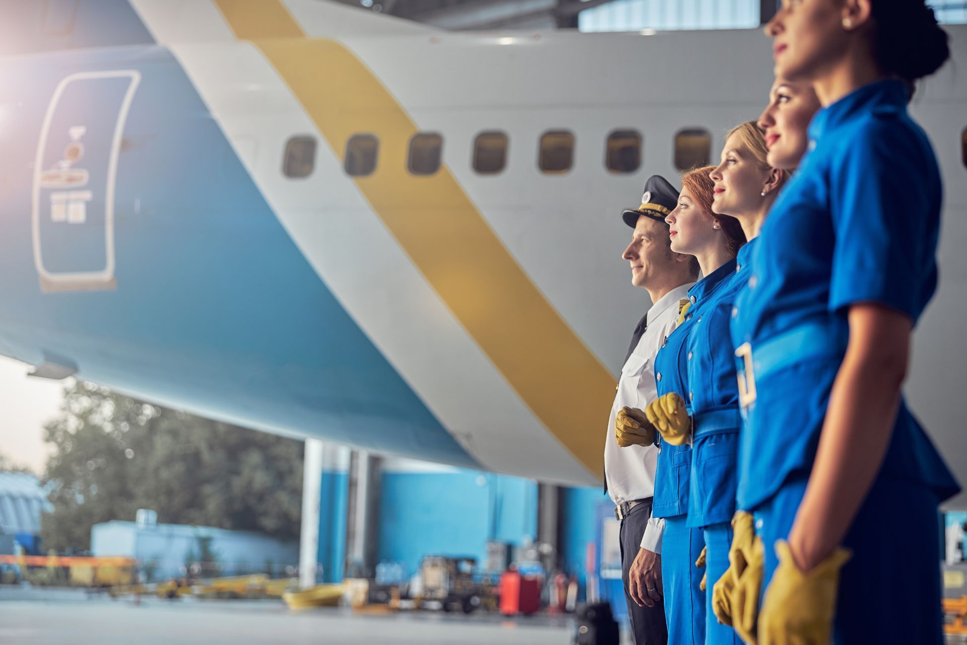 Airport staff in blue uniforms stand beside a plane, looking ahead on the tarmac.