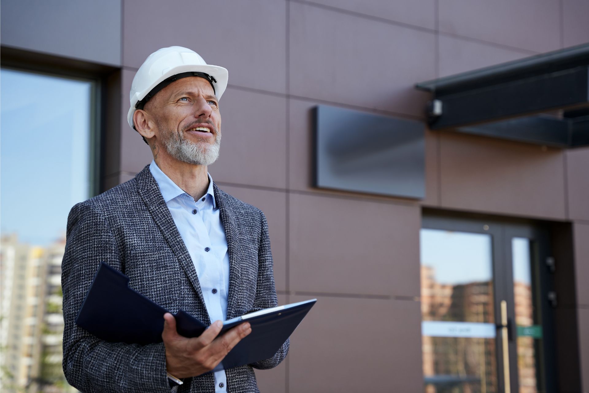 Man in a white hard hat holding a folder outside a modern building