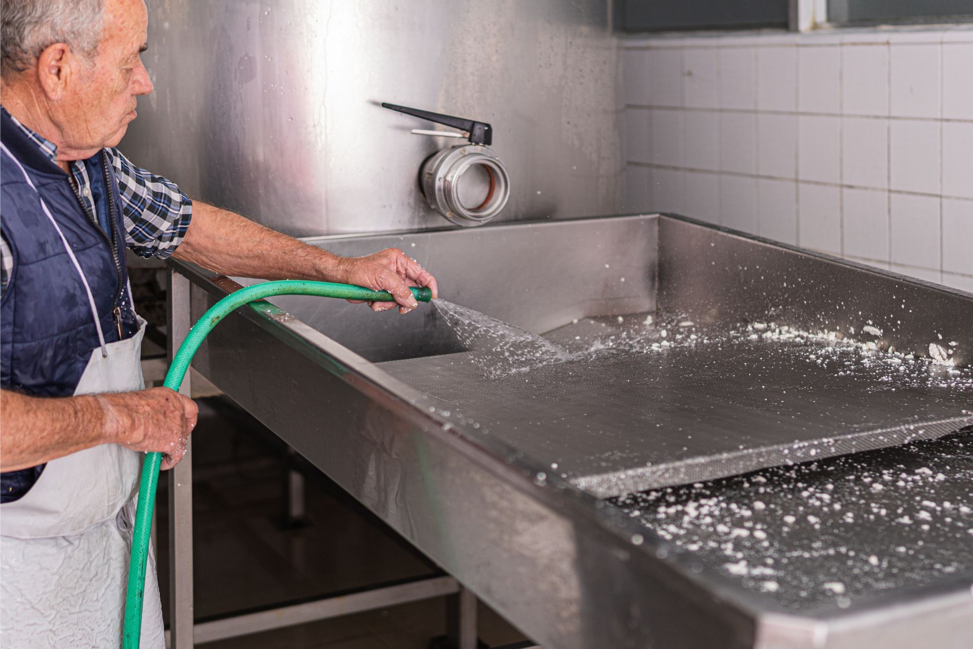 Worker spraying water into a stainless steel industrial sink during cleanup