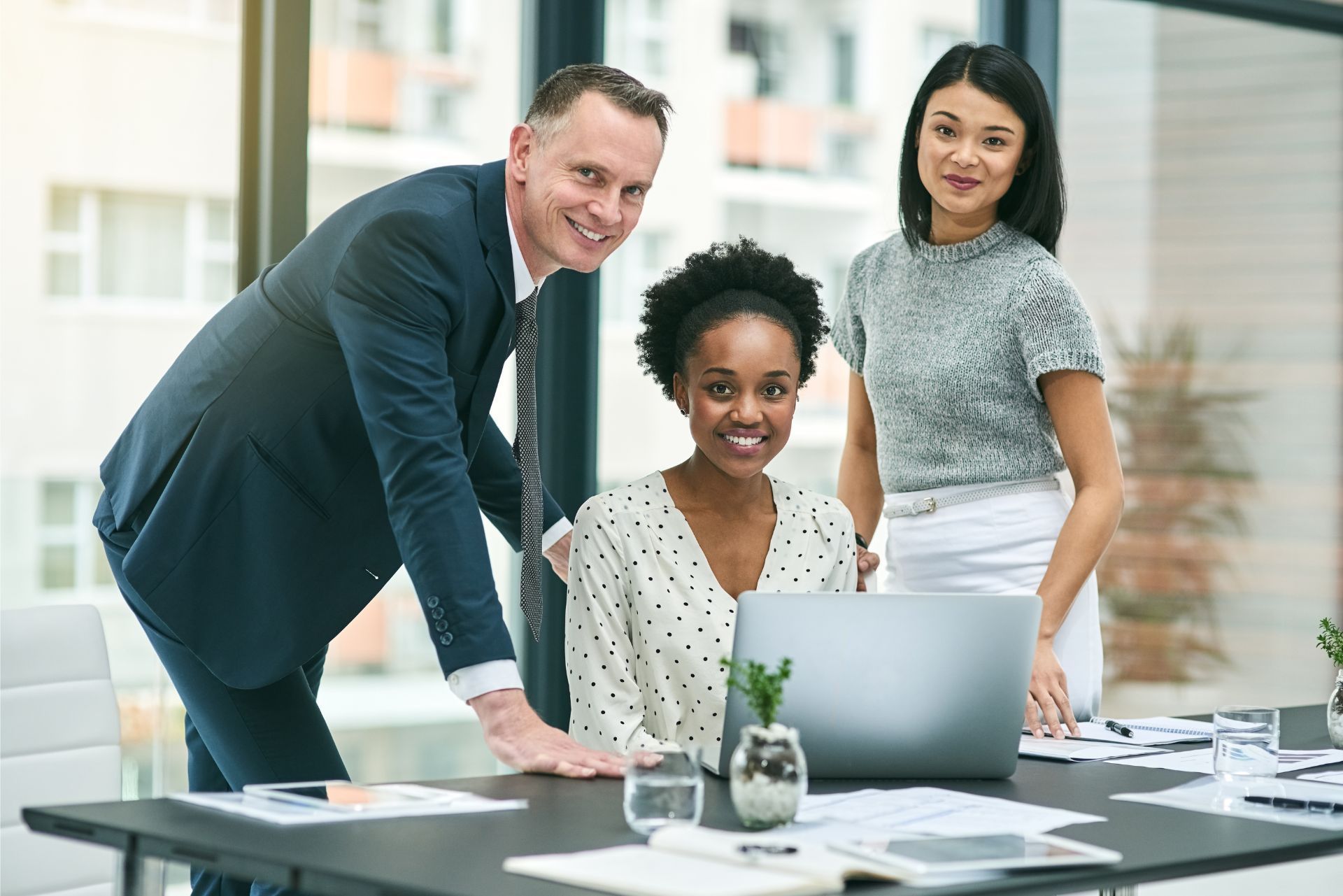 Three coworkers smiling around a laptop in a bright office